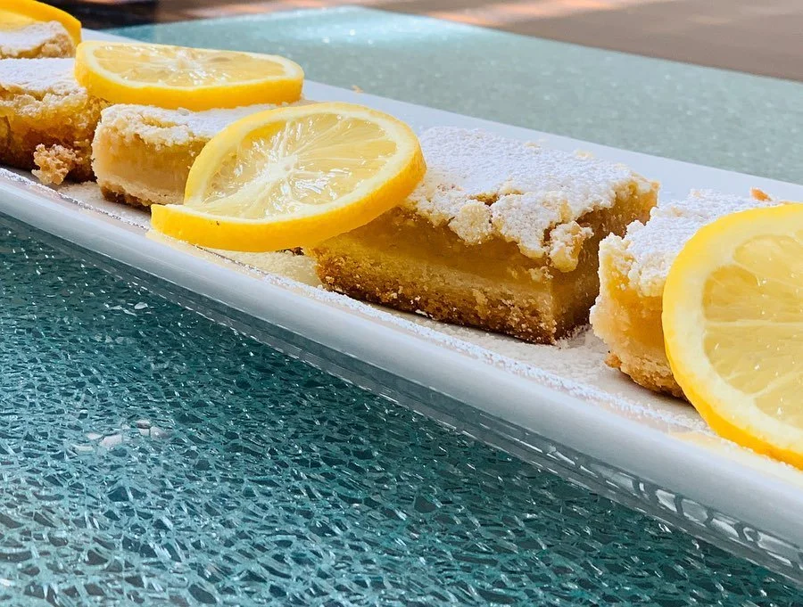 Lemon bars garnished with lemon slices on a white rectangular plate.