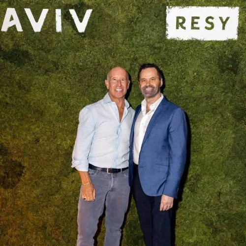 Photo of ceo Barry Sternlicht standing in front of an event set piece. the background reads "Aviv" and "Resy" and he is standing next to another man