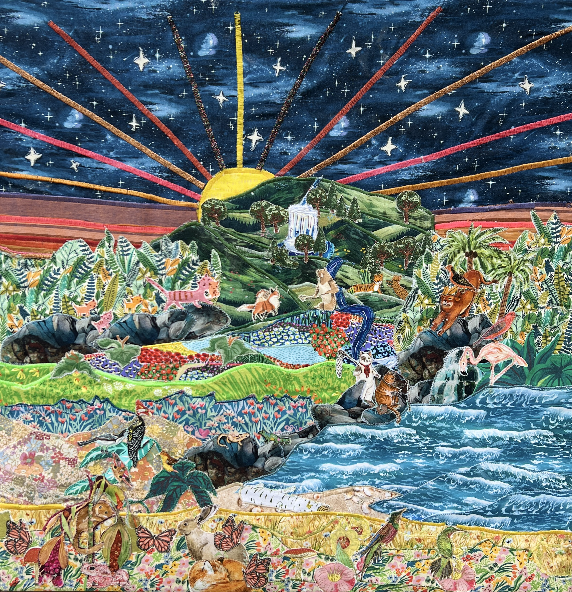 Colorful fabric collage depicting a whimsical landscape with animals, lush greenery, rolling hills, a river, and a starry night sky with a sunrise or sunset.