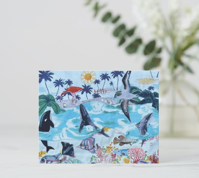 Colorful greeting card featuring a textile collage of a tropical beach scene with palm trees, dolphins jumping in the water, a sunny sky, and various fish and coral along the shoreline.