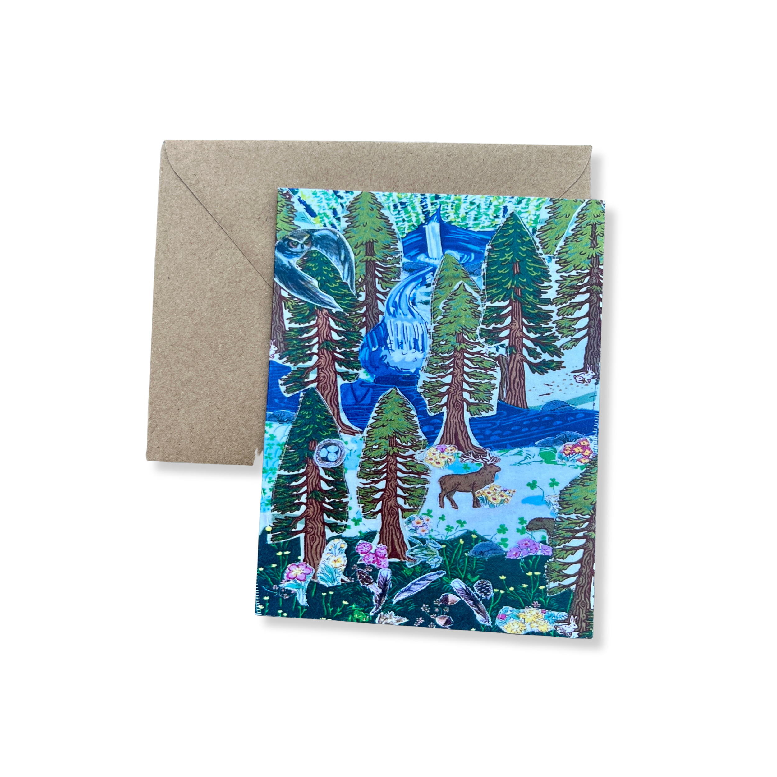 A greeting card  featuring an image of a fabric collage with a scene of a forest with trees, a waterfall, animals including a bear, a moose, birds, and mushrooms in a nature setting, with an envelope