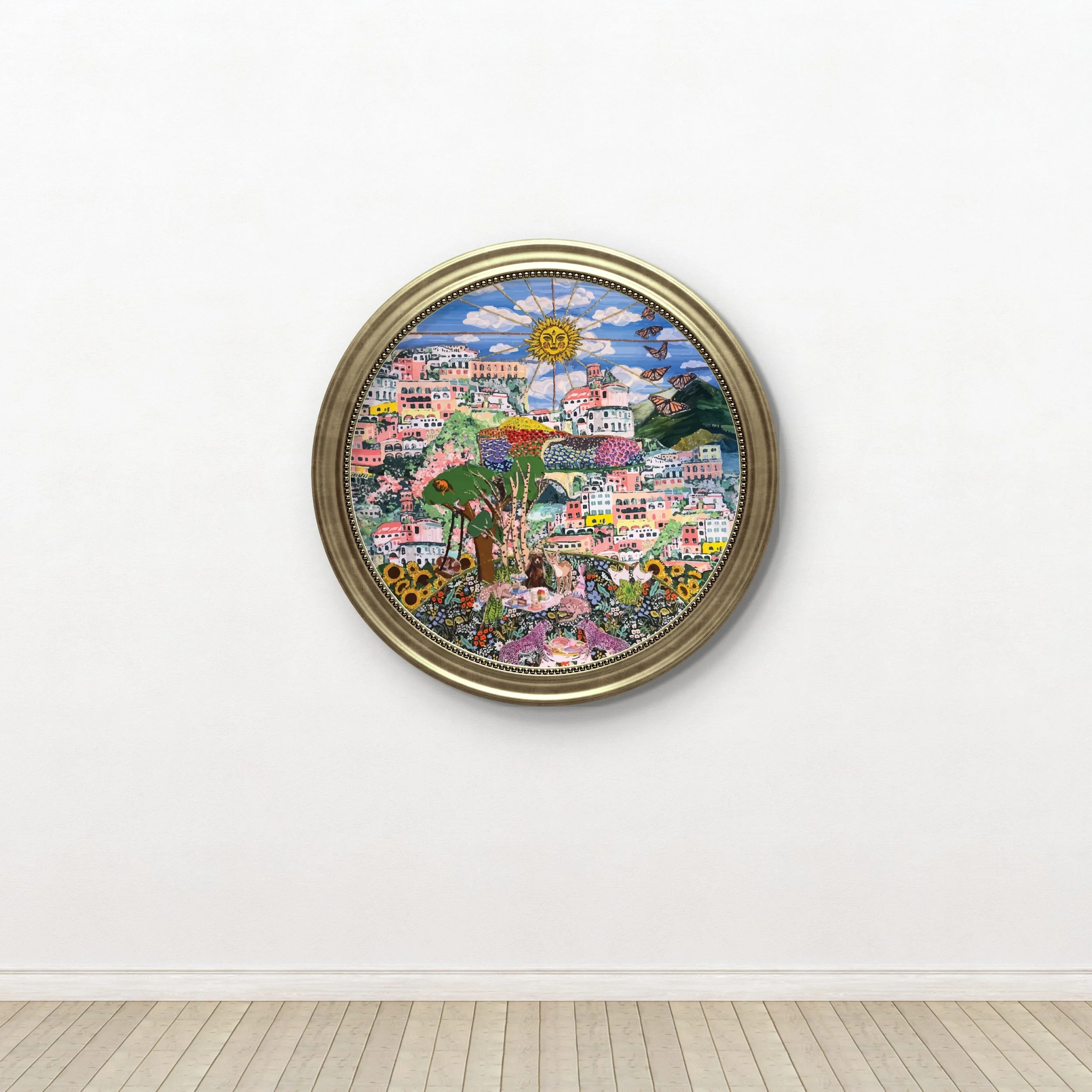 Colorful framed textile collage depicting a hillside town with houses, trees, flowers, a bright sun, and flying butterflies on a white wall.