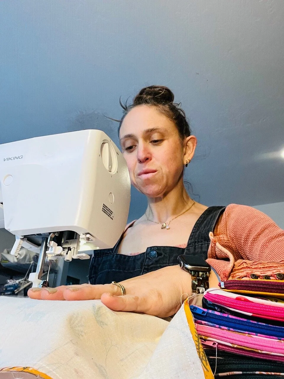 A woman sewing fabric with a Viking sewing machine, focused on her work, with colorful pouches on the desk nearby.
