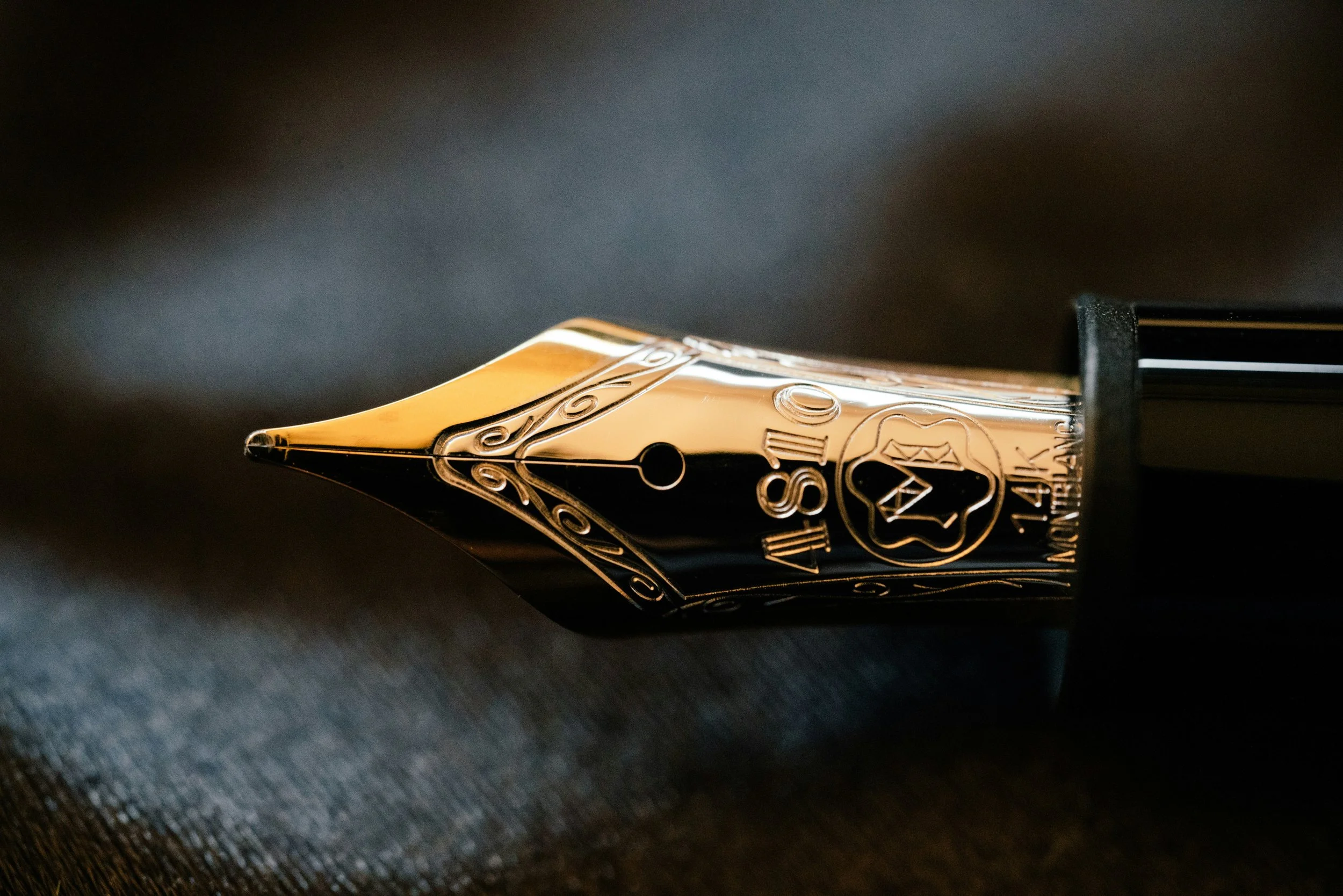 Close-up of a gold and black fountain pen nib resting on a dark surface.