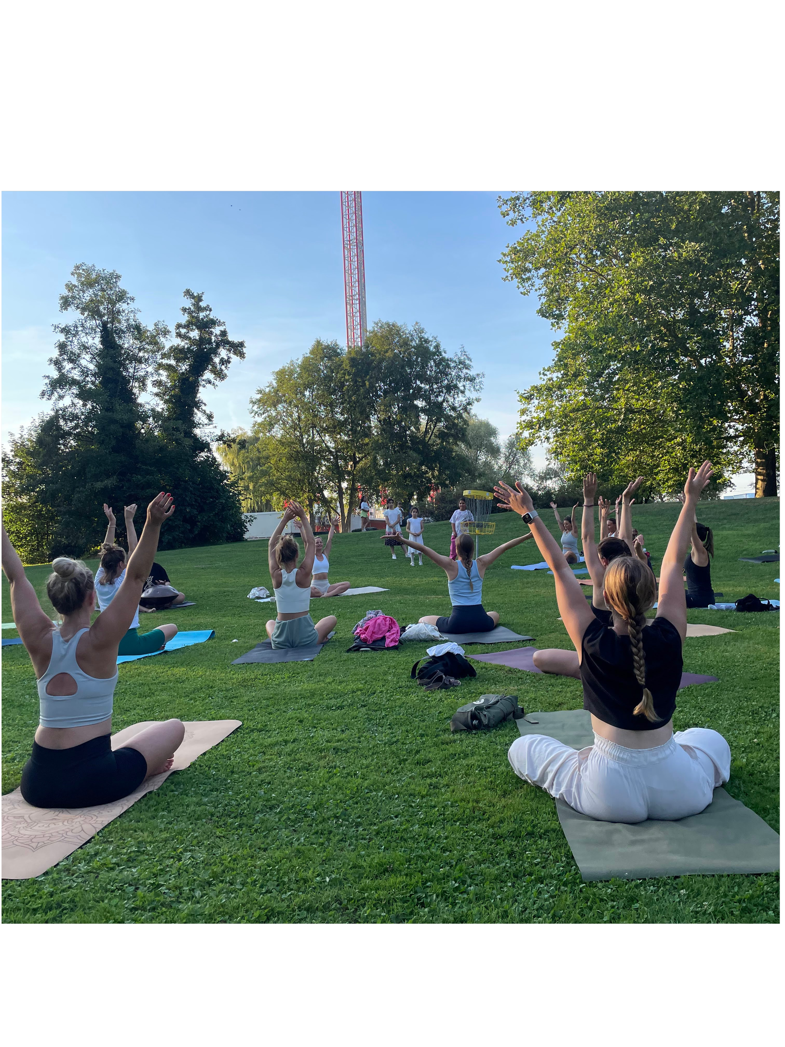Menschen beim Yoga im Freien auf einer Wiese unter Bäumen bei sonnigem Wetter. Outdoor Yoga