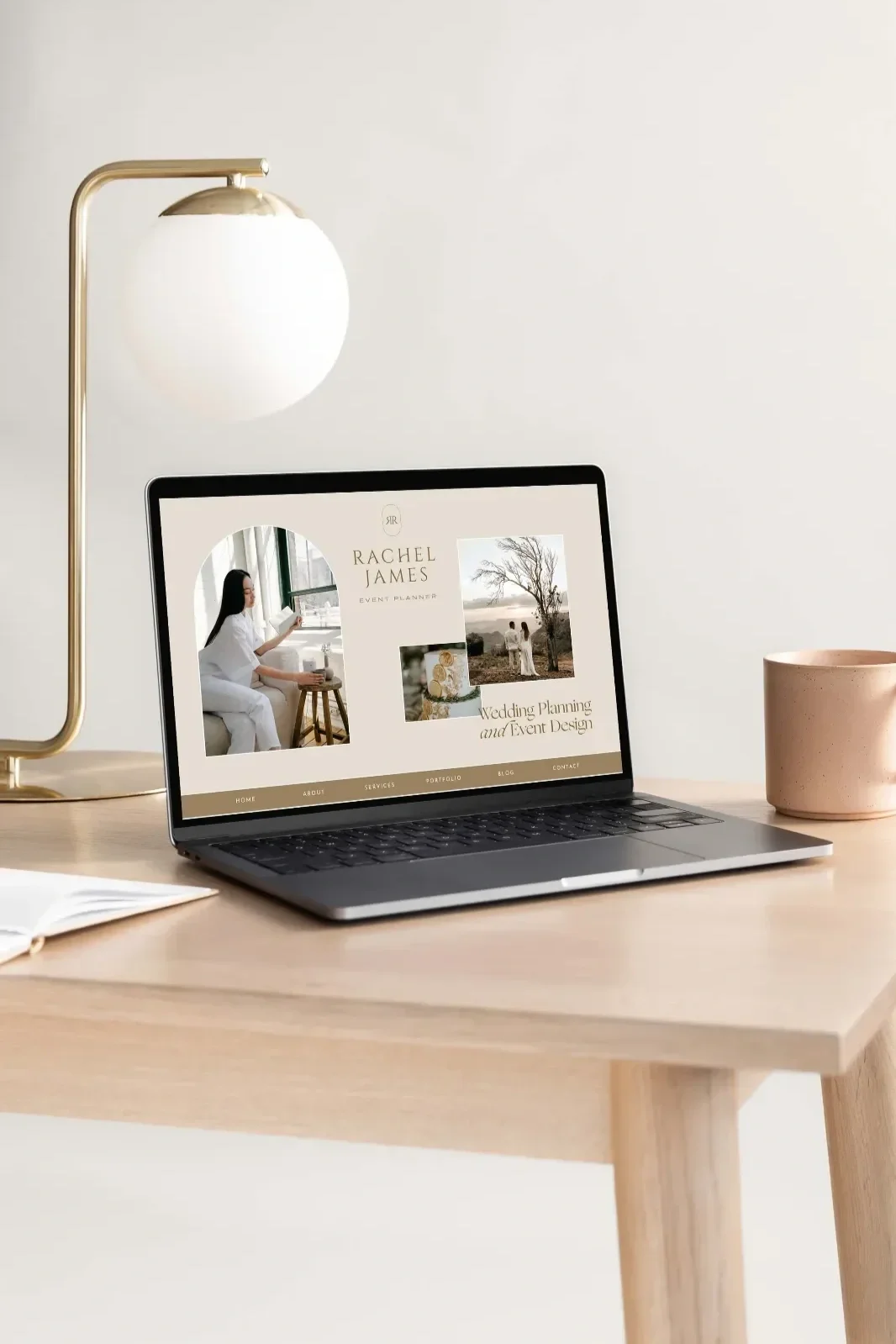 Laptop displaying a wedding planning website named Rachel James on a wooden desk with a table lamp, a pink mug, and an open notebook in a minimal, modern office setting.
