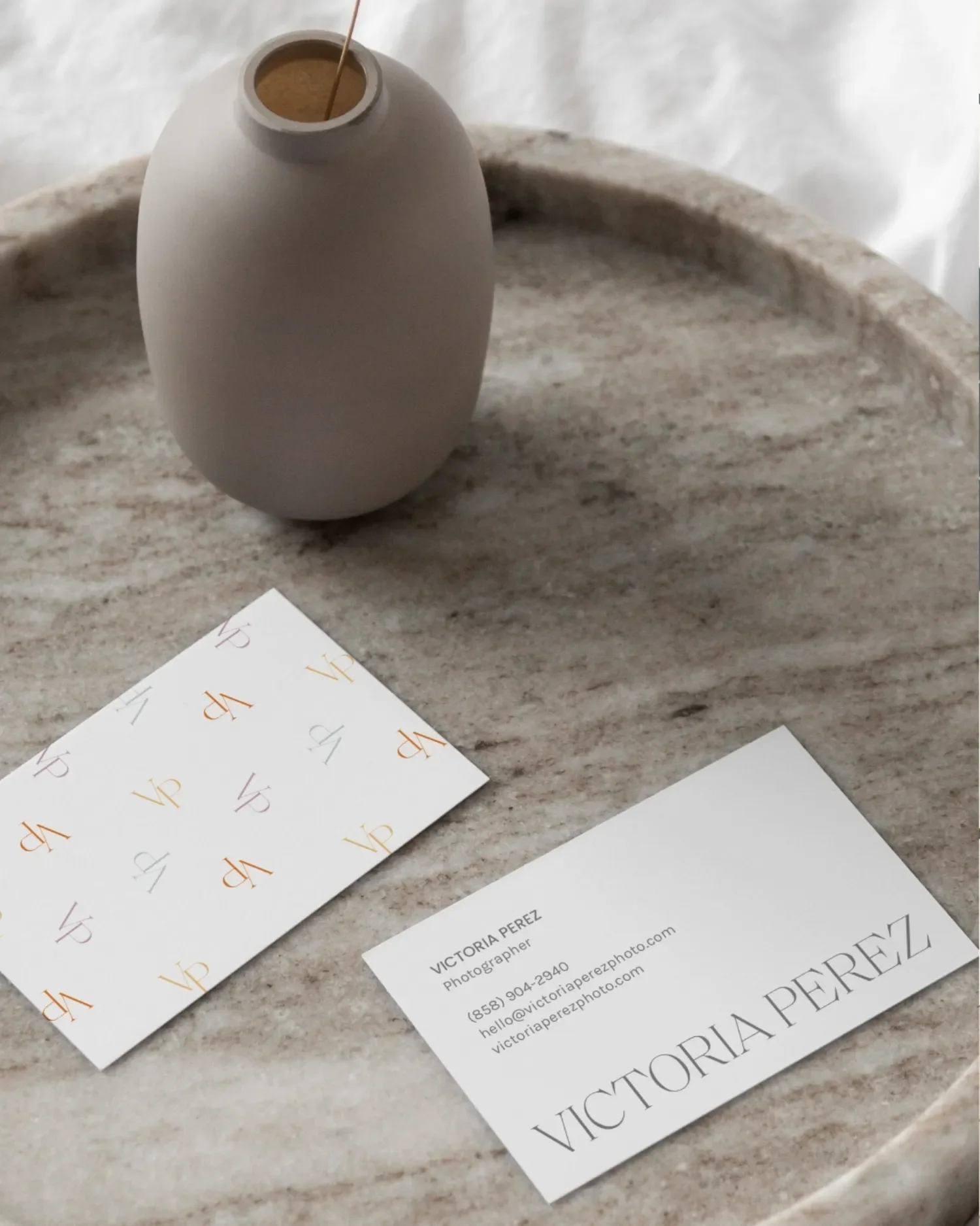 Business cards on a marble surface with a white ceramic vase, and business card details for Victoria Perez, a photographer, including email and phone number.