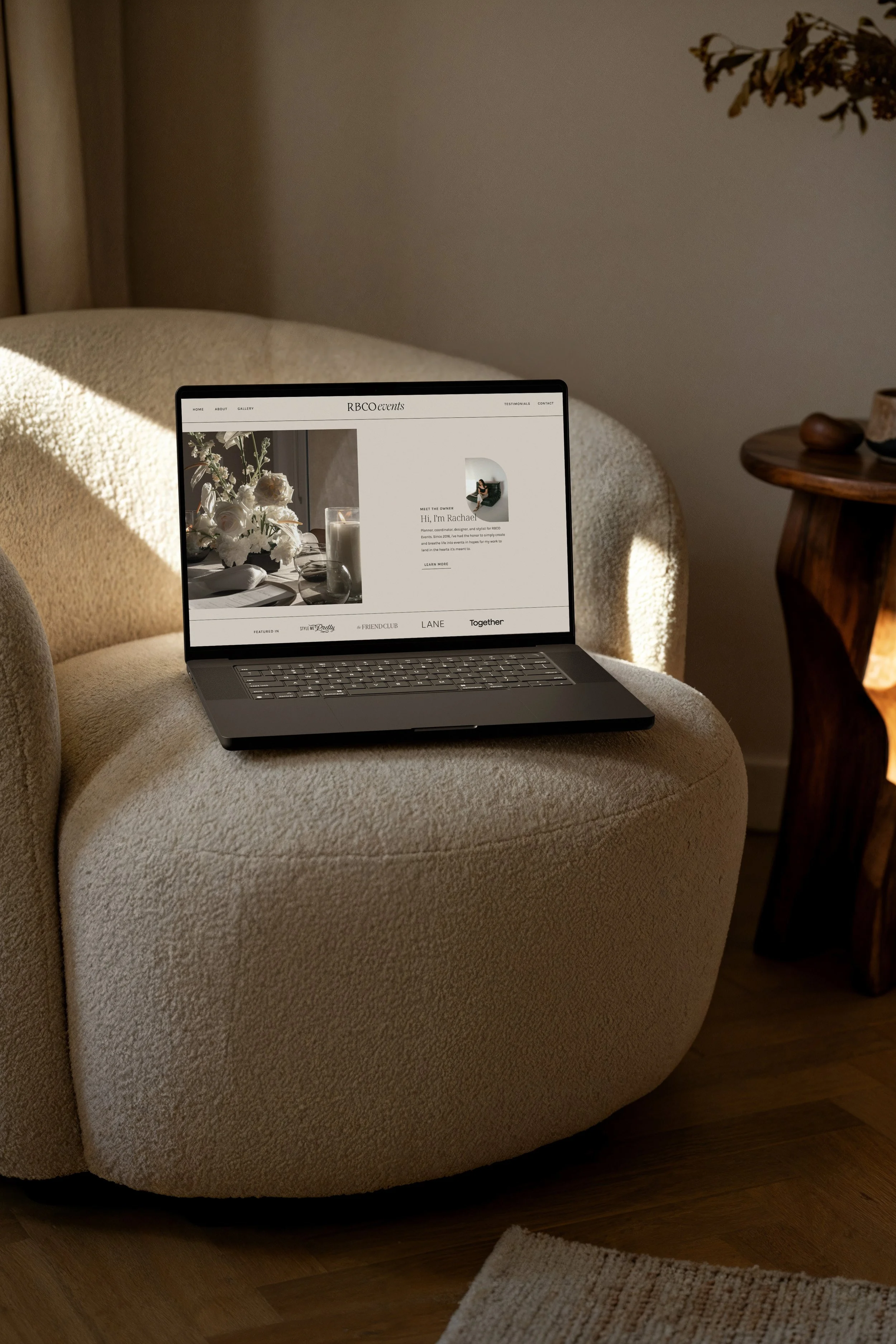 A laptop placed on a plush beige armchair in a cozy living room with a wooden side table next to it.