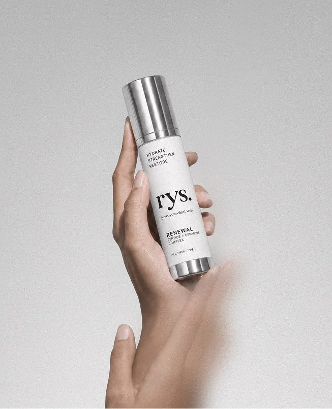 A hand holding a skincare bottle labeled 'rys' against a plain background.