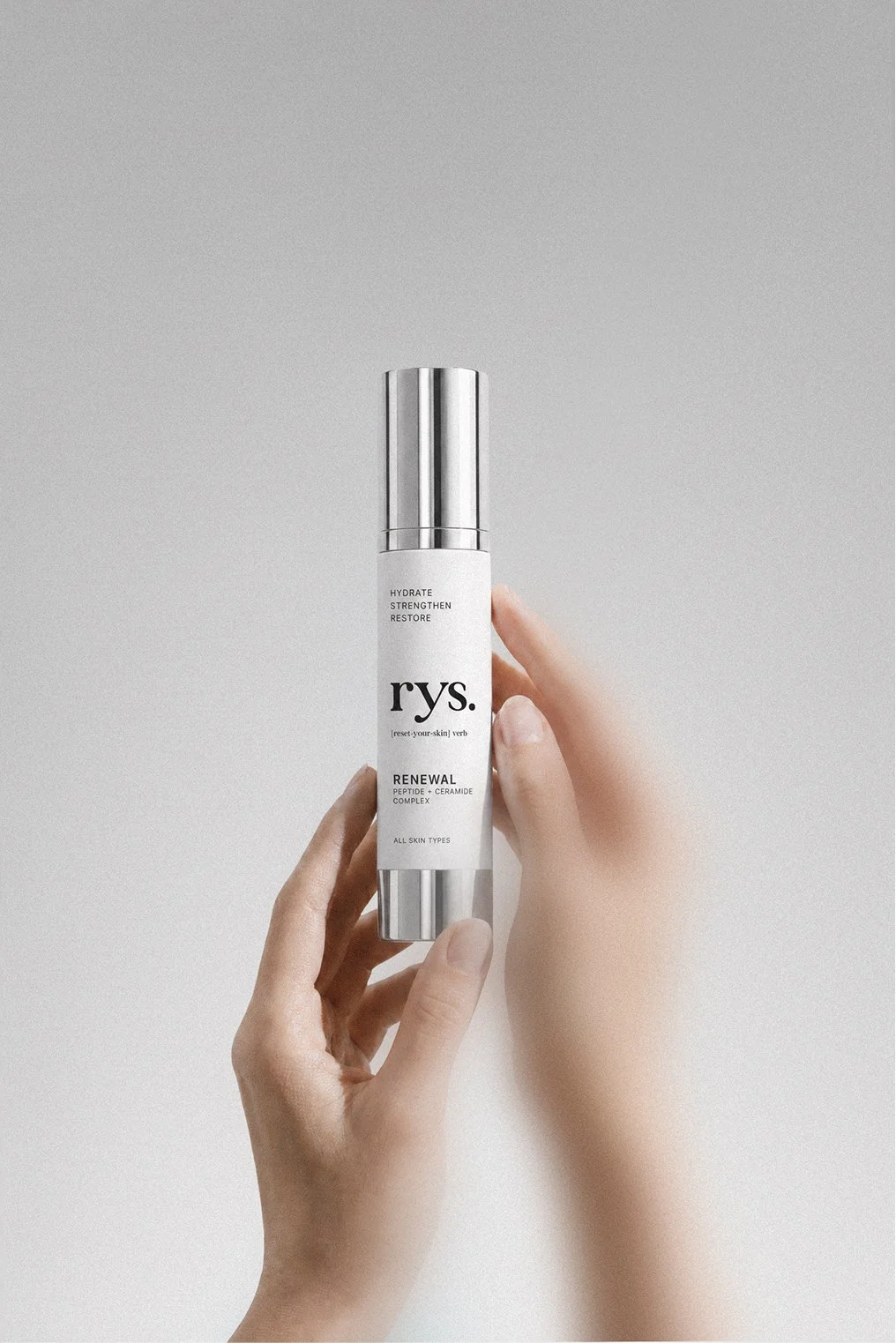 Hand holding a skincare product bottle against a plain light gray background.
