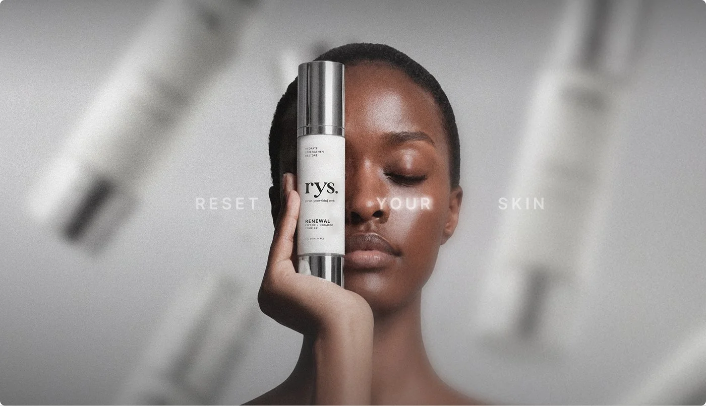 A woman with short hair holds a bottle of Skin Renewing Serum up to her face, with the words 'RESET YOUR SKIN' faintly visible in the background.