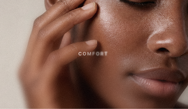 Close-up of a woman's face with her eyes closed, gently touching her cheek with her finger, and the word 'COMFORT' overlaid near her cheek.
