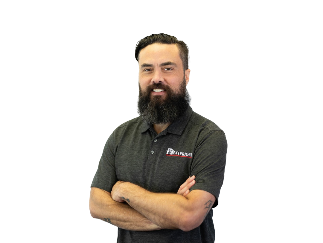 Young man with short black hair and a full black beard smiling at the camera with his arms crossed, wearing a branded grey polo style shirt, against a white background.