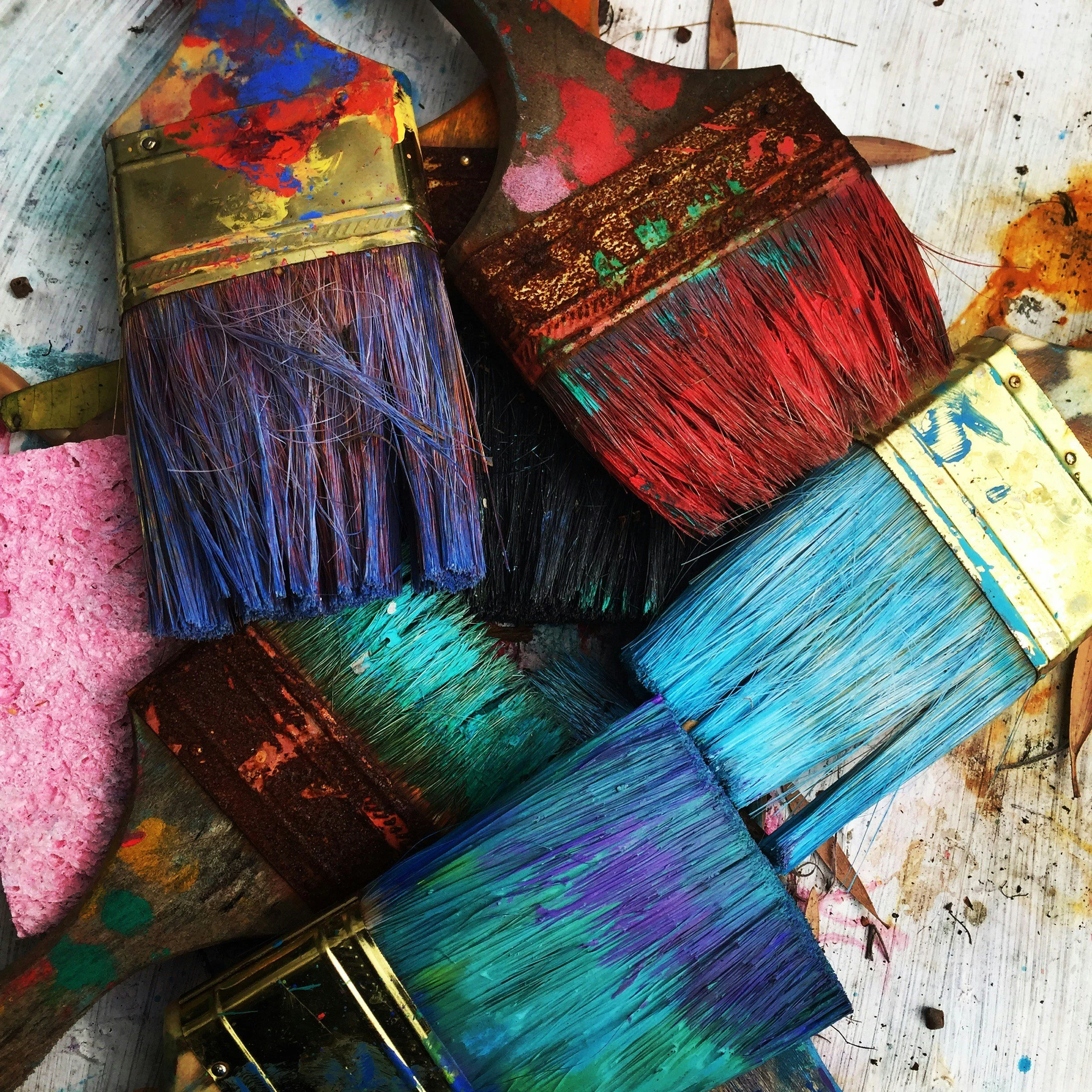 A collection of used paintbrushes with colorful paint on their bristles, resting on a paint-stained surface.
