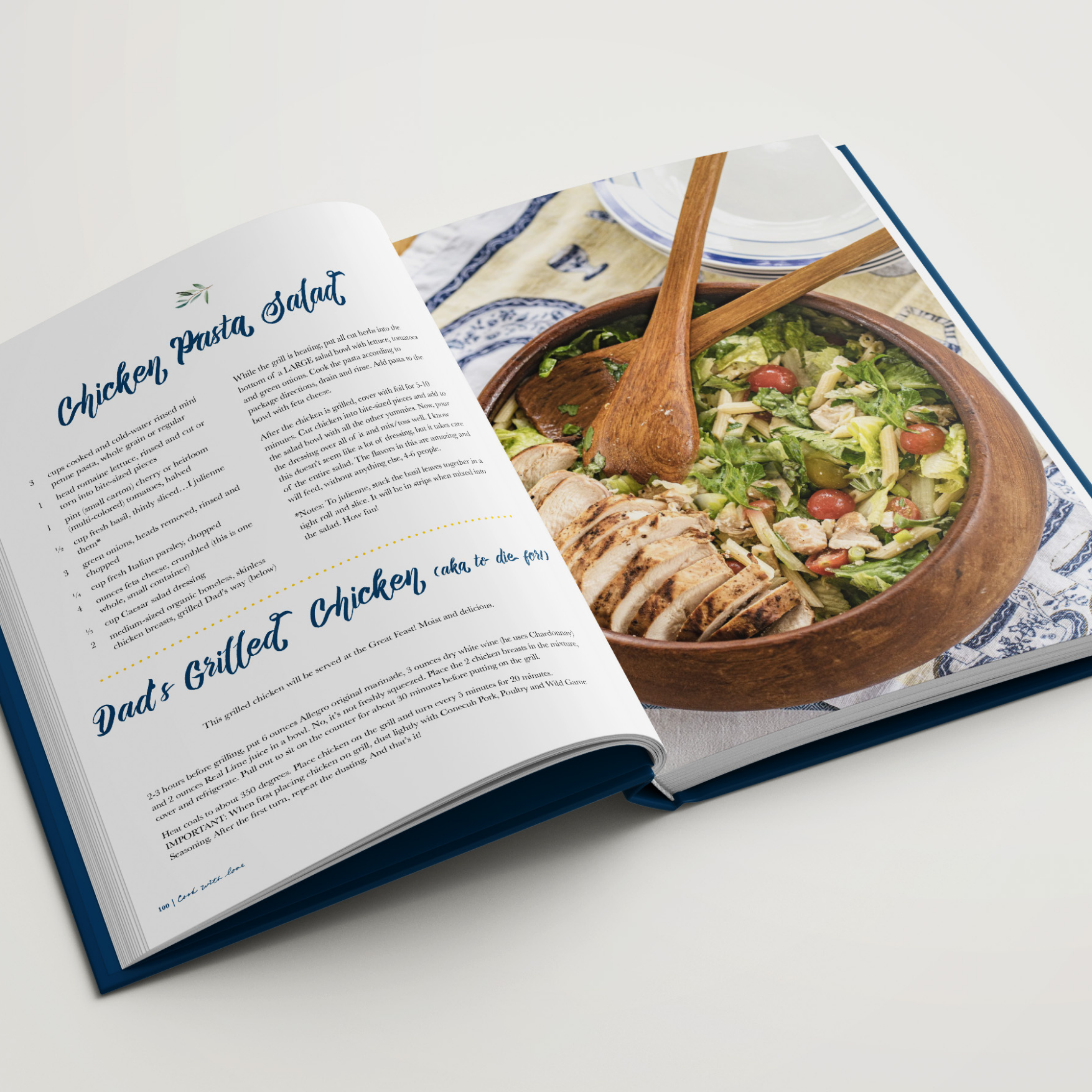 Open cookbook with a chicken salad recipe and grilled chicken pictured on the right page in a wooden bowl with salad tongs.