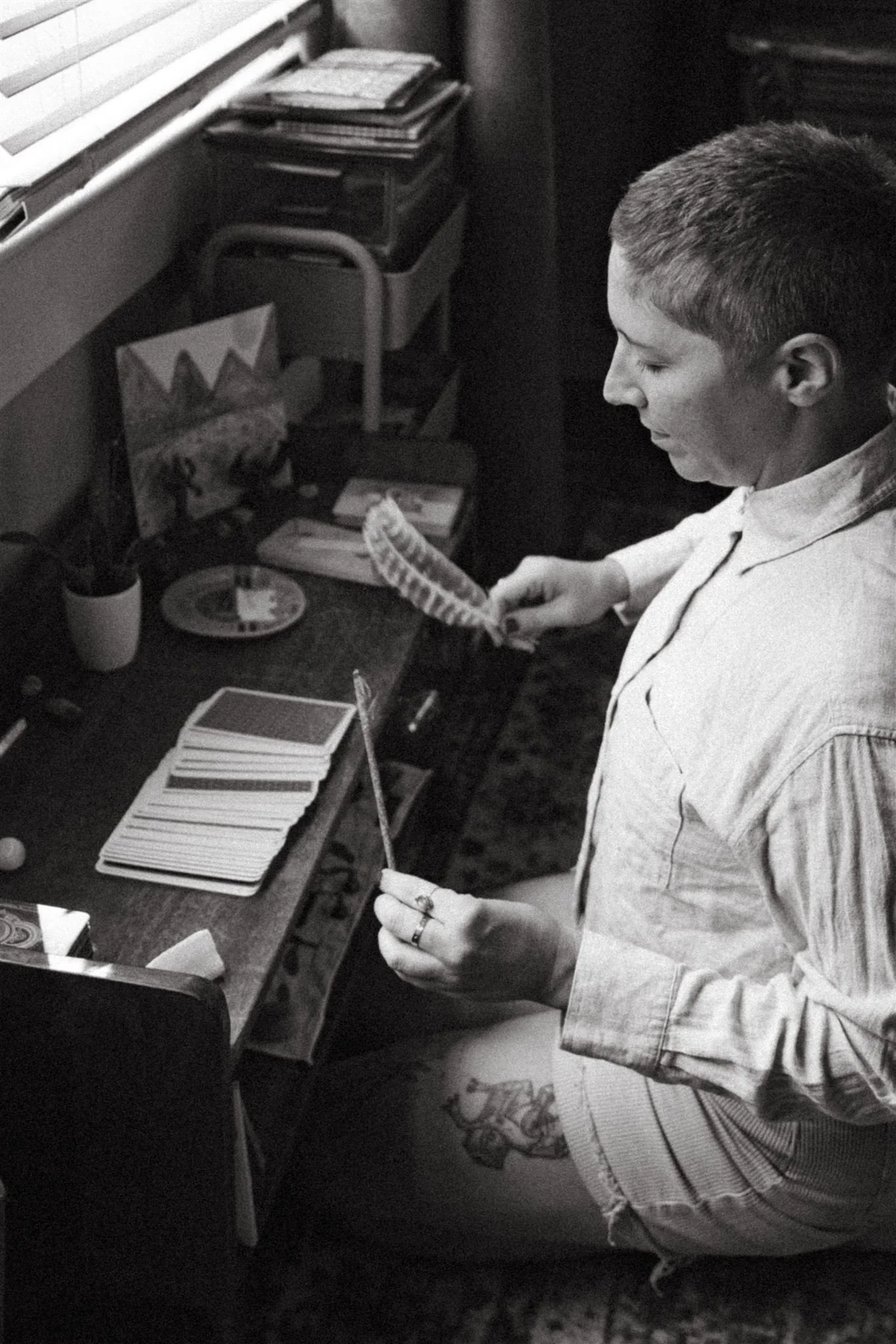 A man sitting at a desk, looking at several playing cards laid out in chess-like fashion, holding two cards in his hands.