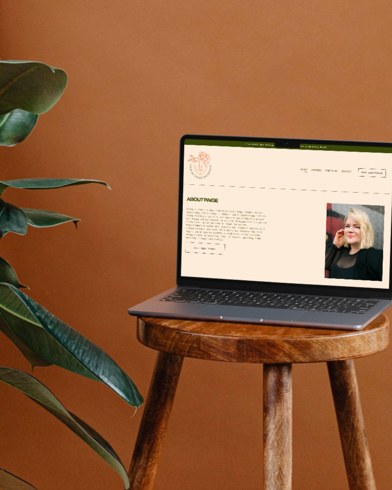 A laptop on a wooden stool displaying a personal website with a photo of a woman and an 'About Paige' section, next to a green plant on a brown wall background.