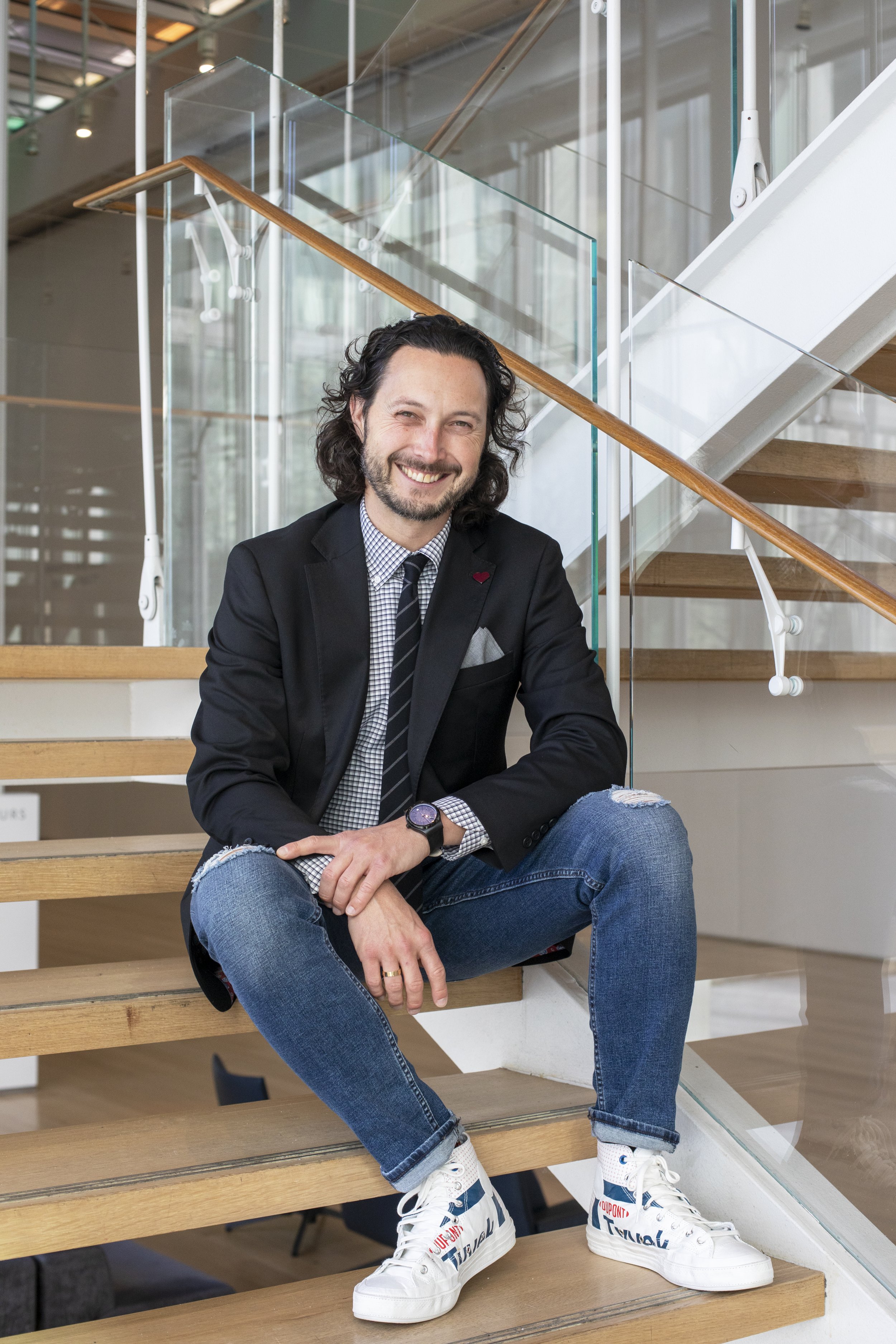 Dr. Tommy Zakrzewski sitting on some steps, wearing a black sport coat, jeans, and white sneakers.