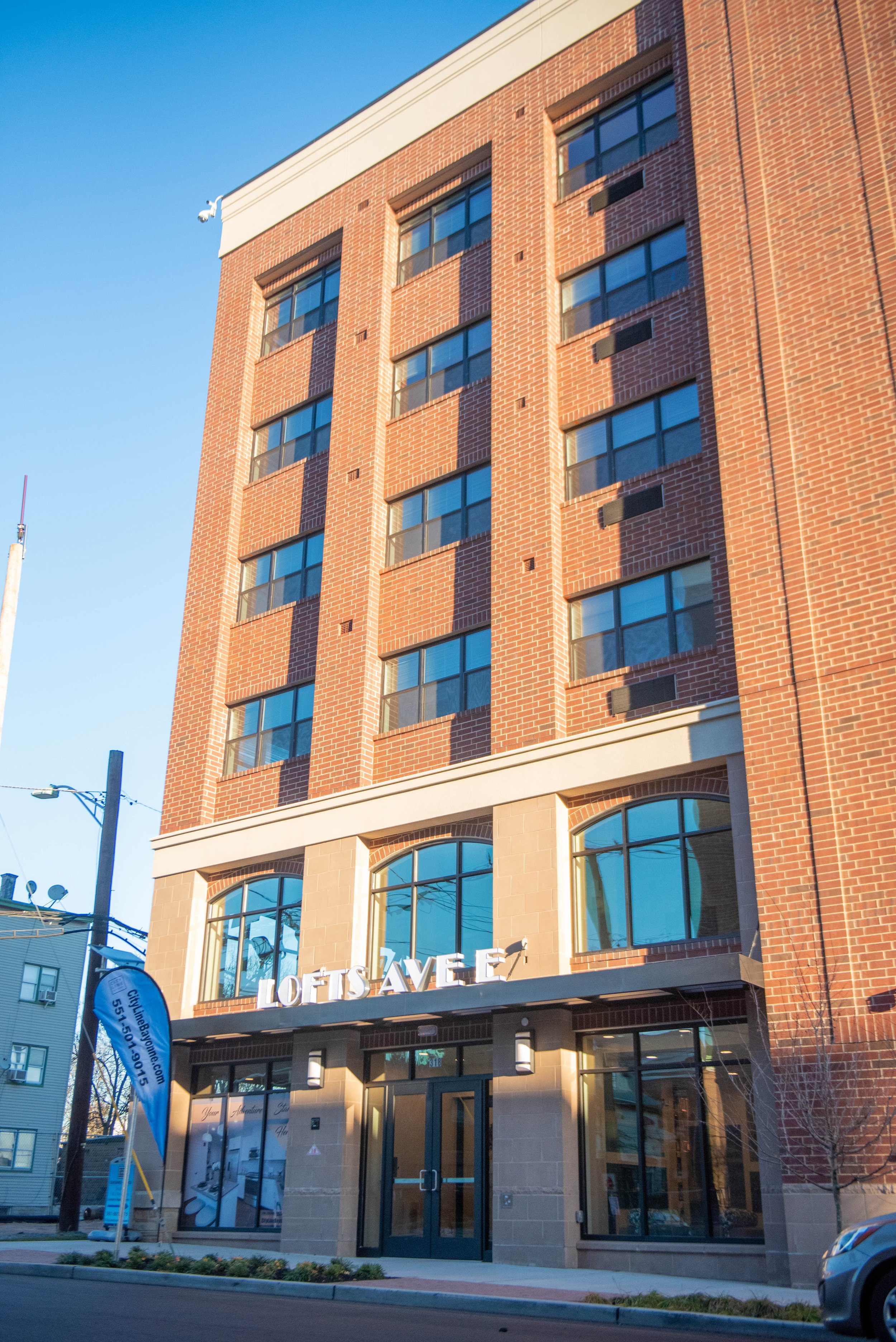 A tall brick building with large windows and a sign that reads 'LOFTS AVE' on the front.