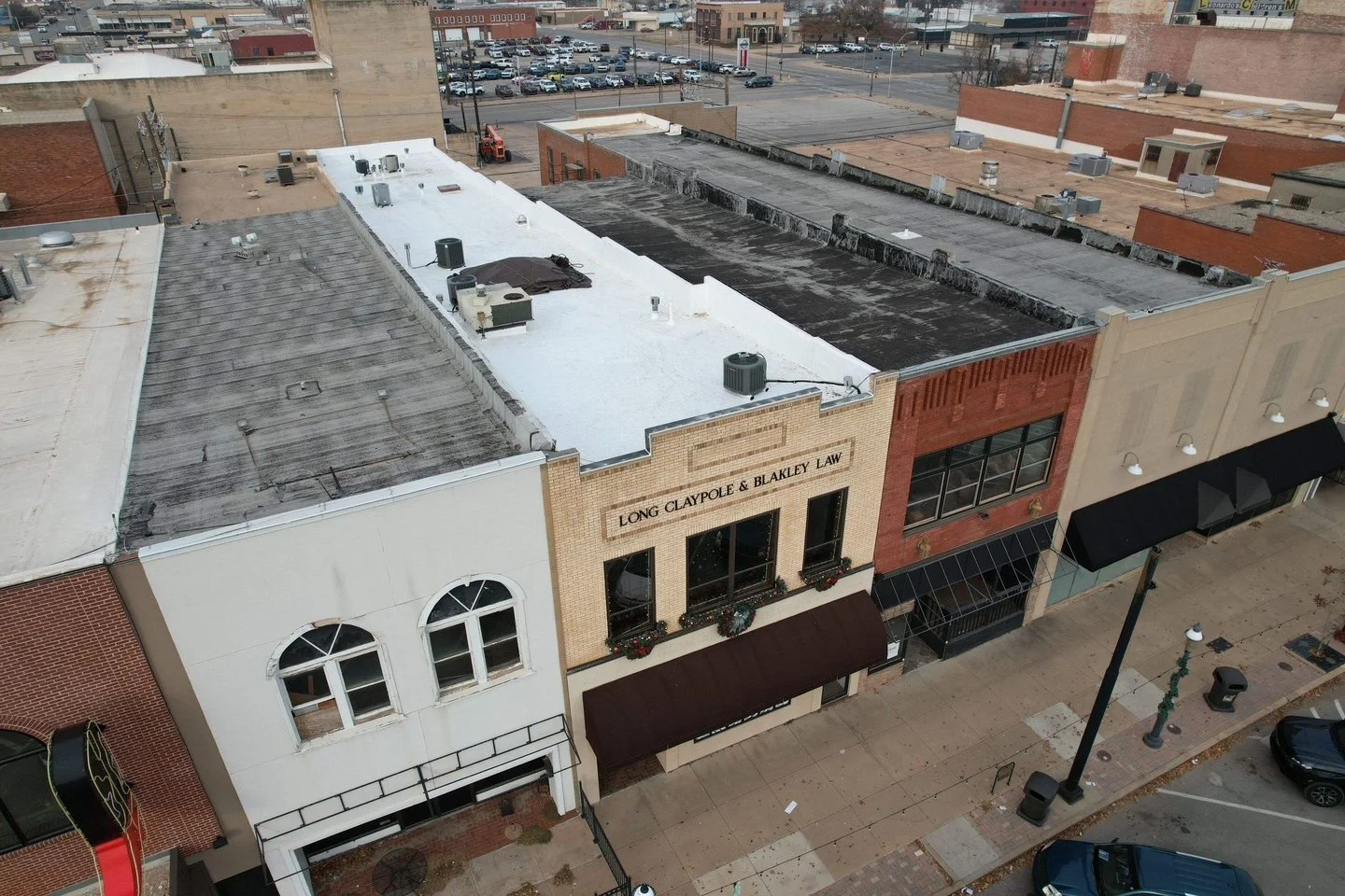 An aerial view of a small downtown area with multiple businesses, including a law firm named Long Claypole & Blakley Law, located in a row of brick and stucco buildings along the sidewalk. The street is lined with parked cars and street lamps.