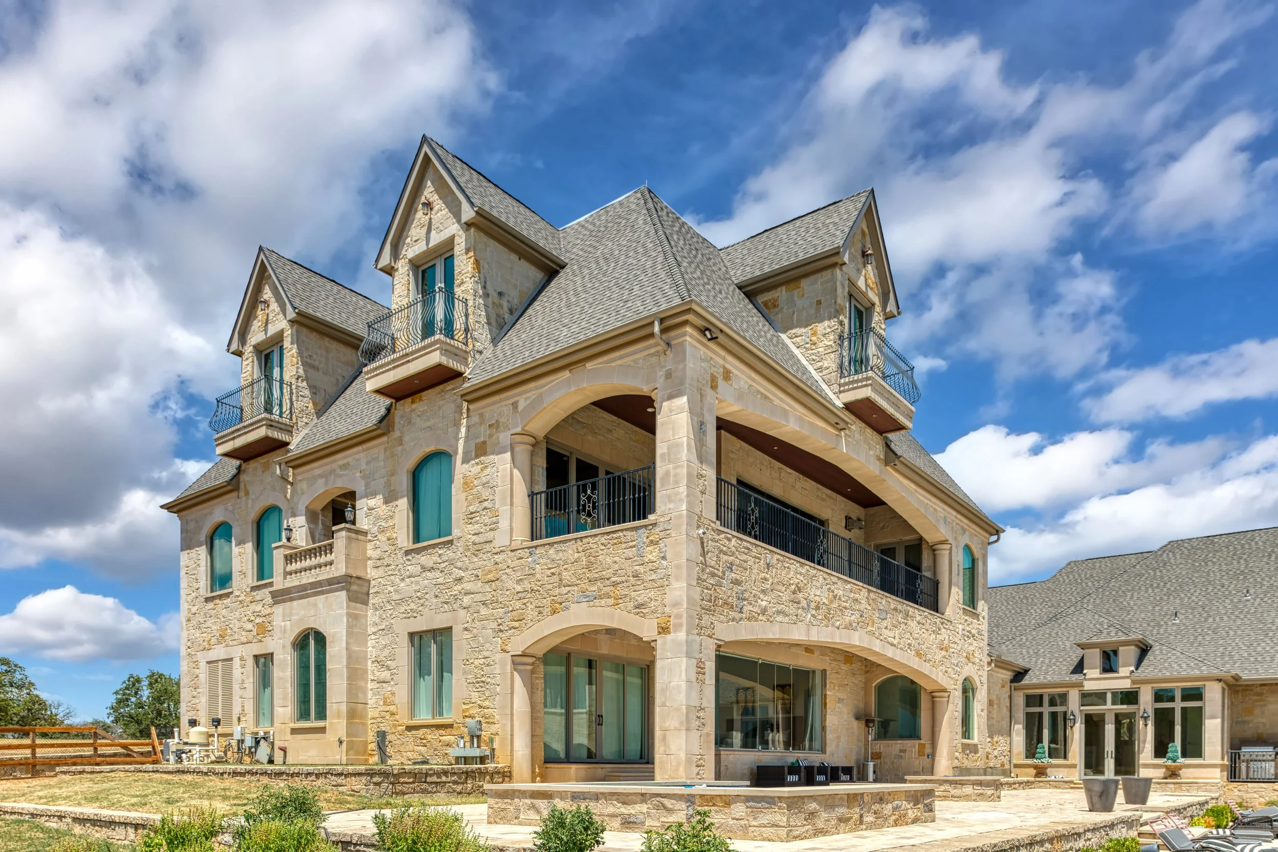 A large stone mansion with multiple levels, balconies, and arched windows, under a partly cloudy sky.