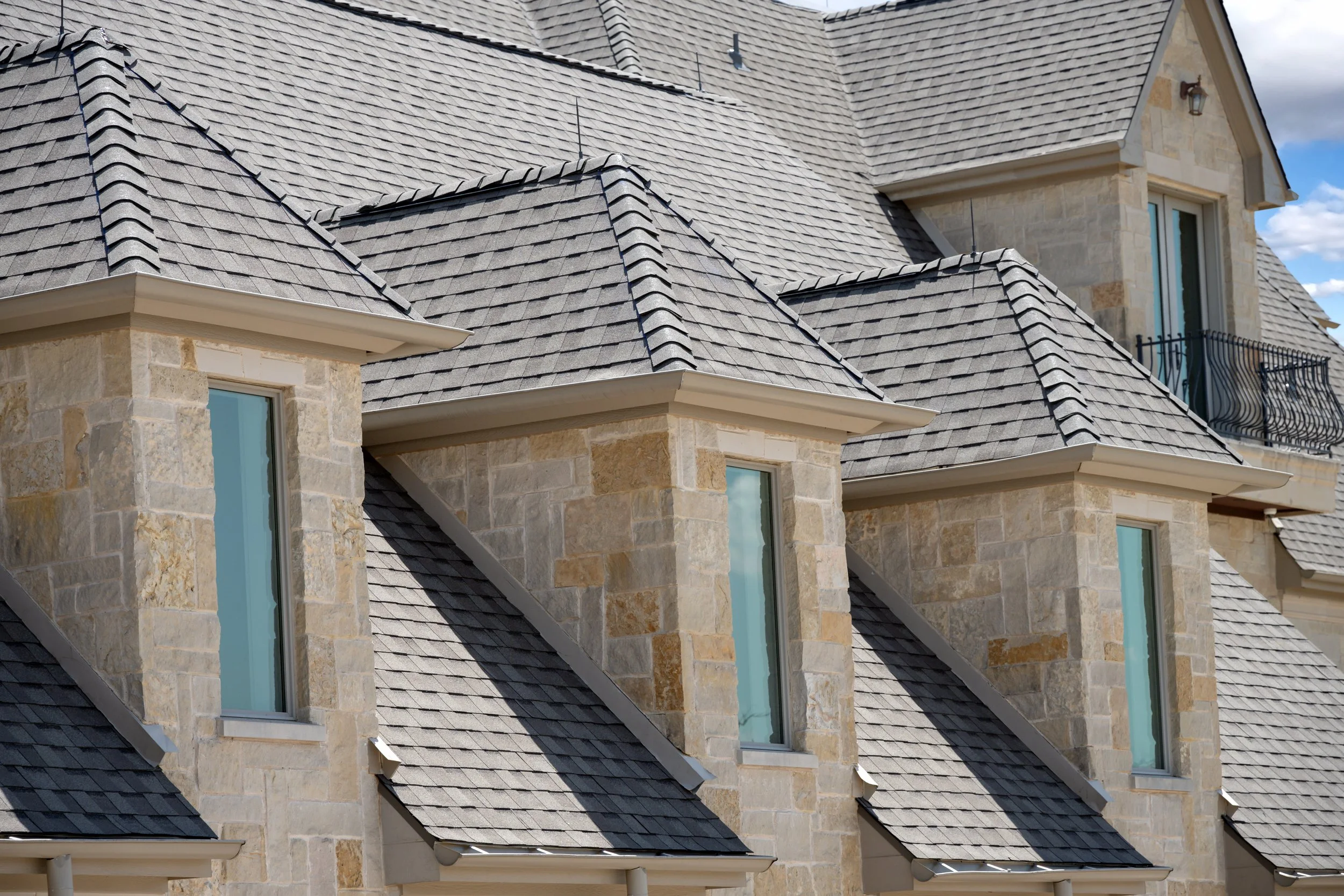Close-up of a multi-story stone house with dormer windows and a slate roof.