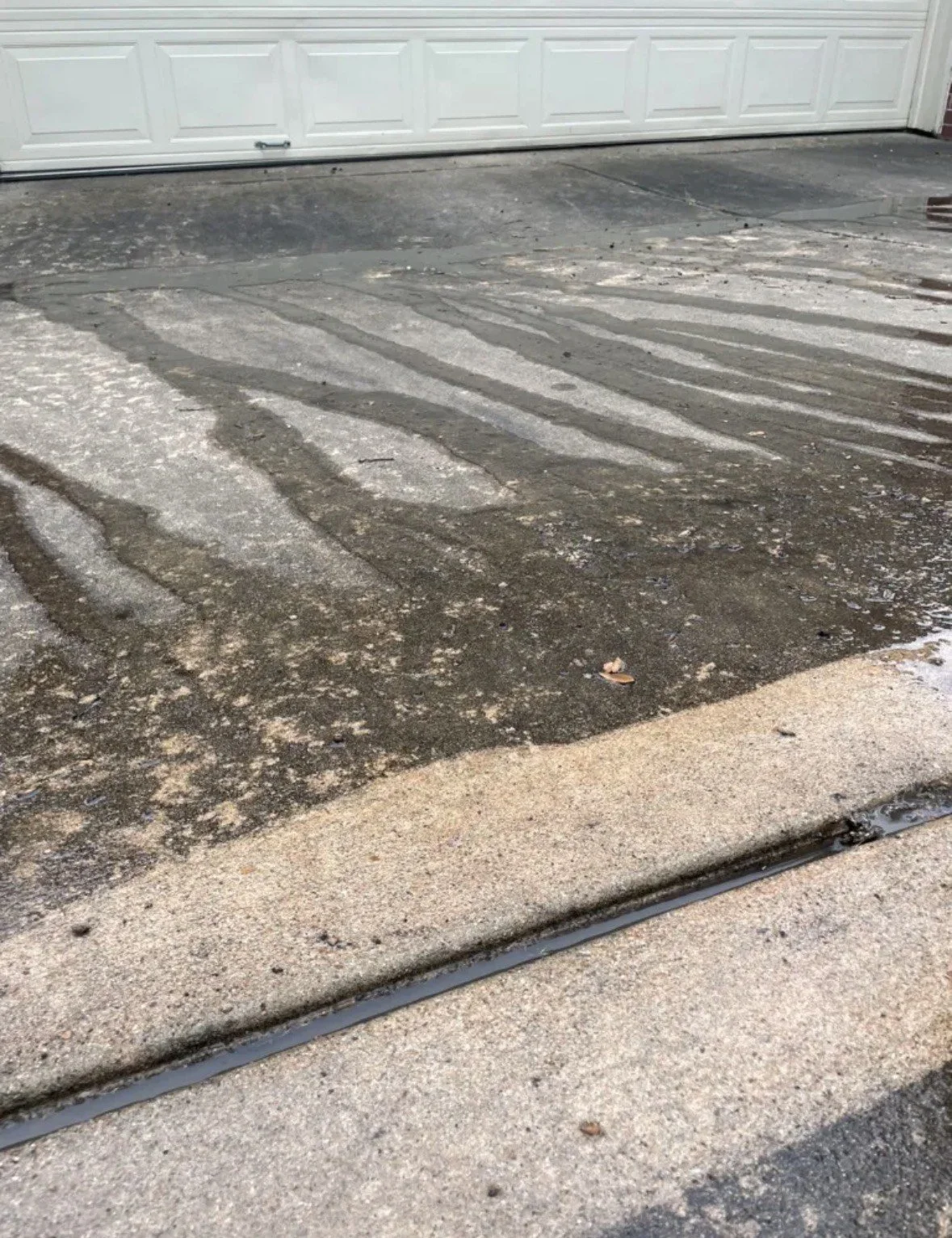 Dirty concrete driveway with streaks from tracked mud and a closed white garage door in the background.