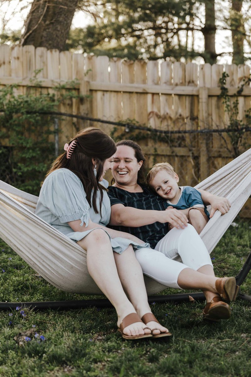 lesbian family sitting together laughing in a hammock
