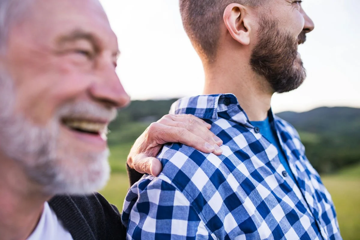 father and his adult son smiling looking at sunset together