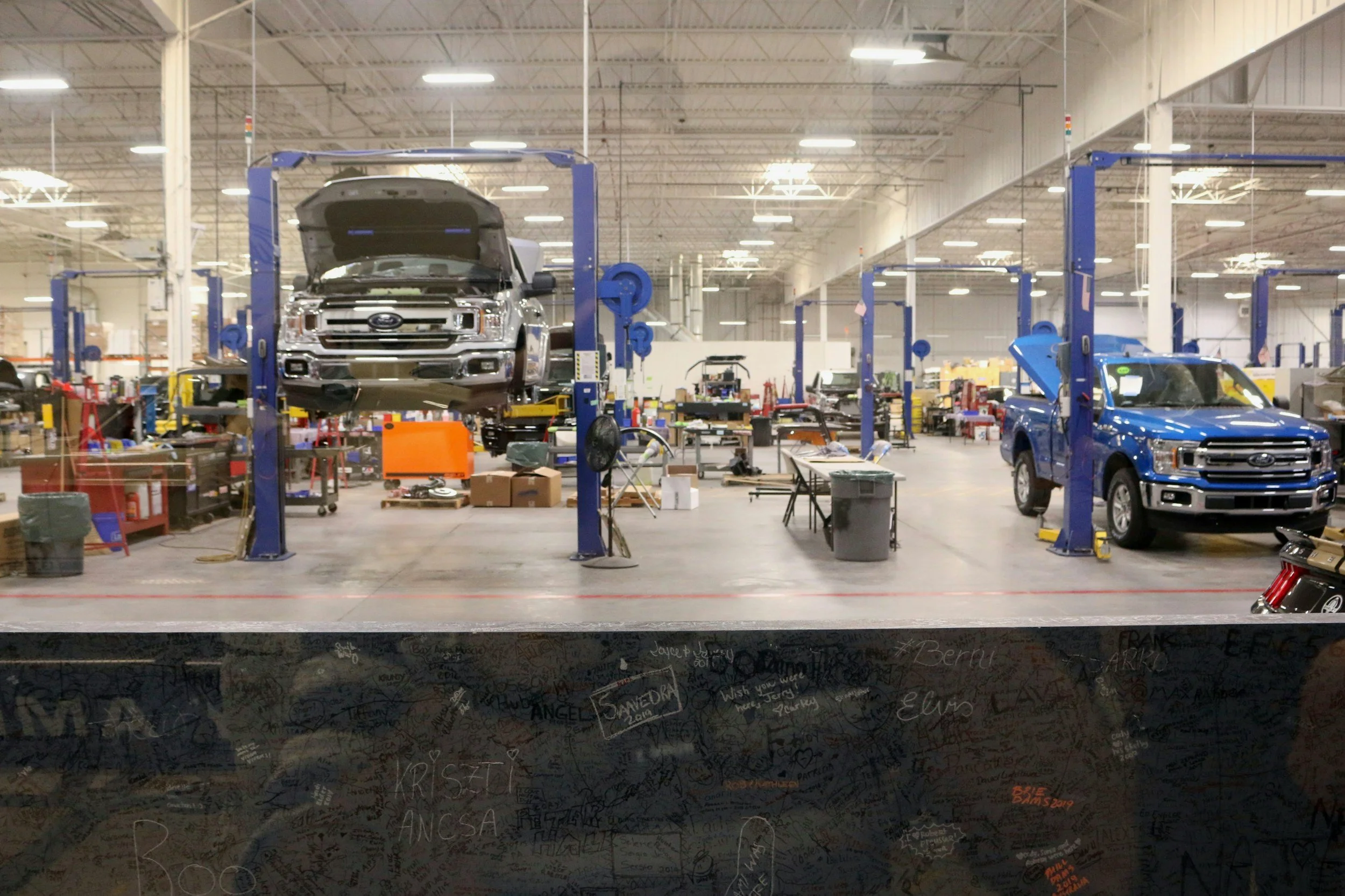 Two Ford trucks on hydraulic lifts in an automotive repair shop, with tools and equipment scattered around.