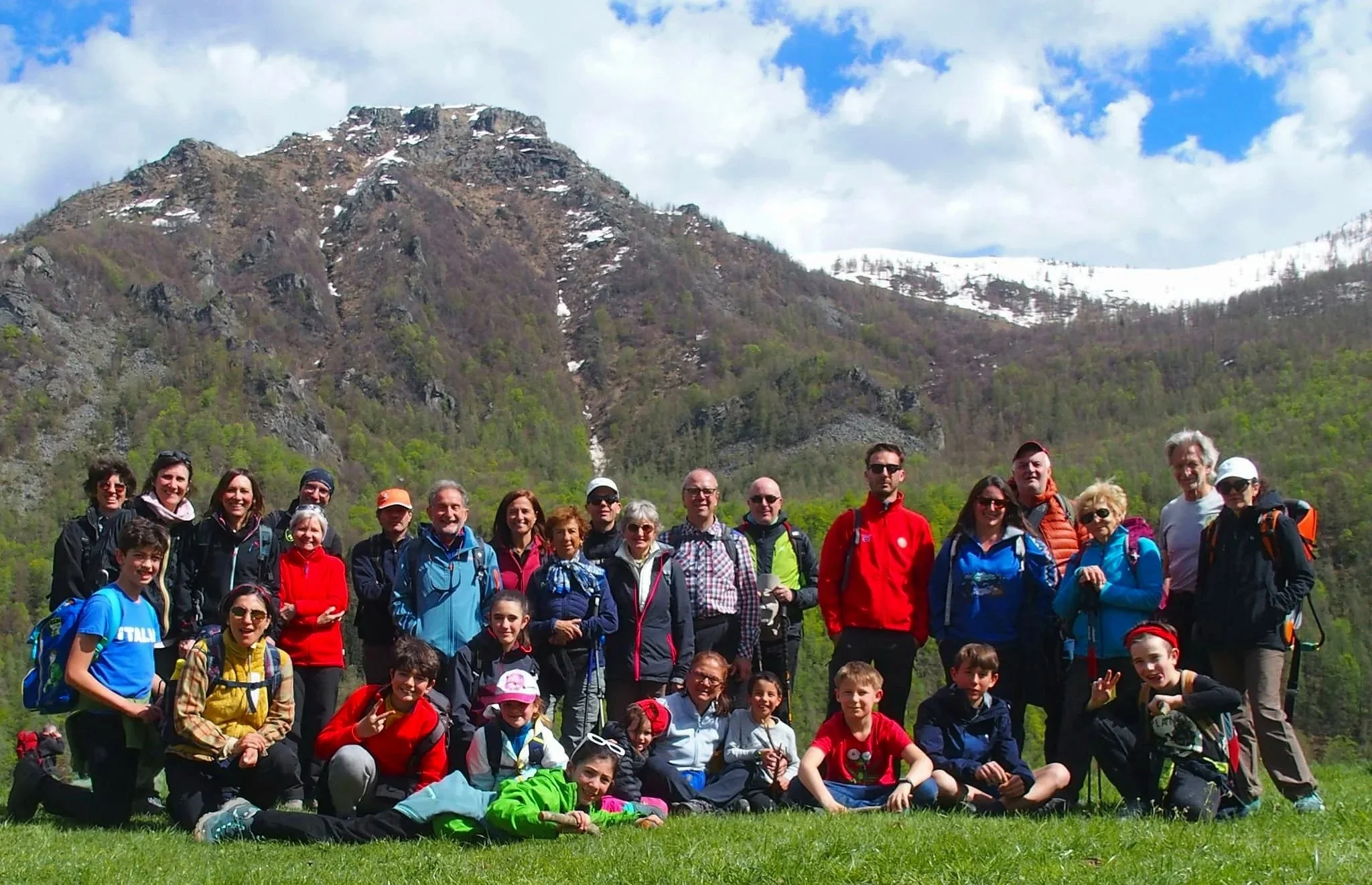 Gruppo di persone, adulti e bambini, in escursione in montagna con neve sulla cima, cielo nuvoloso