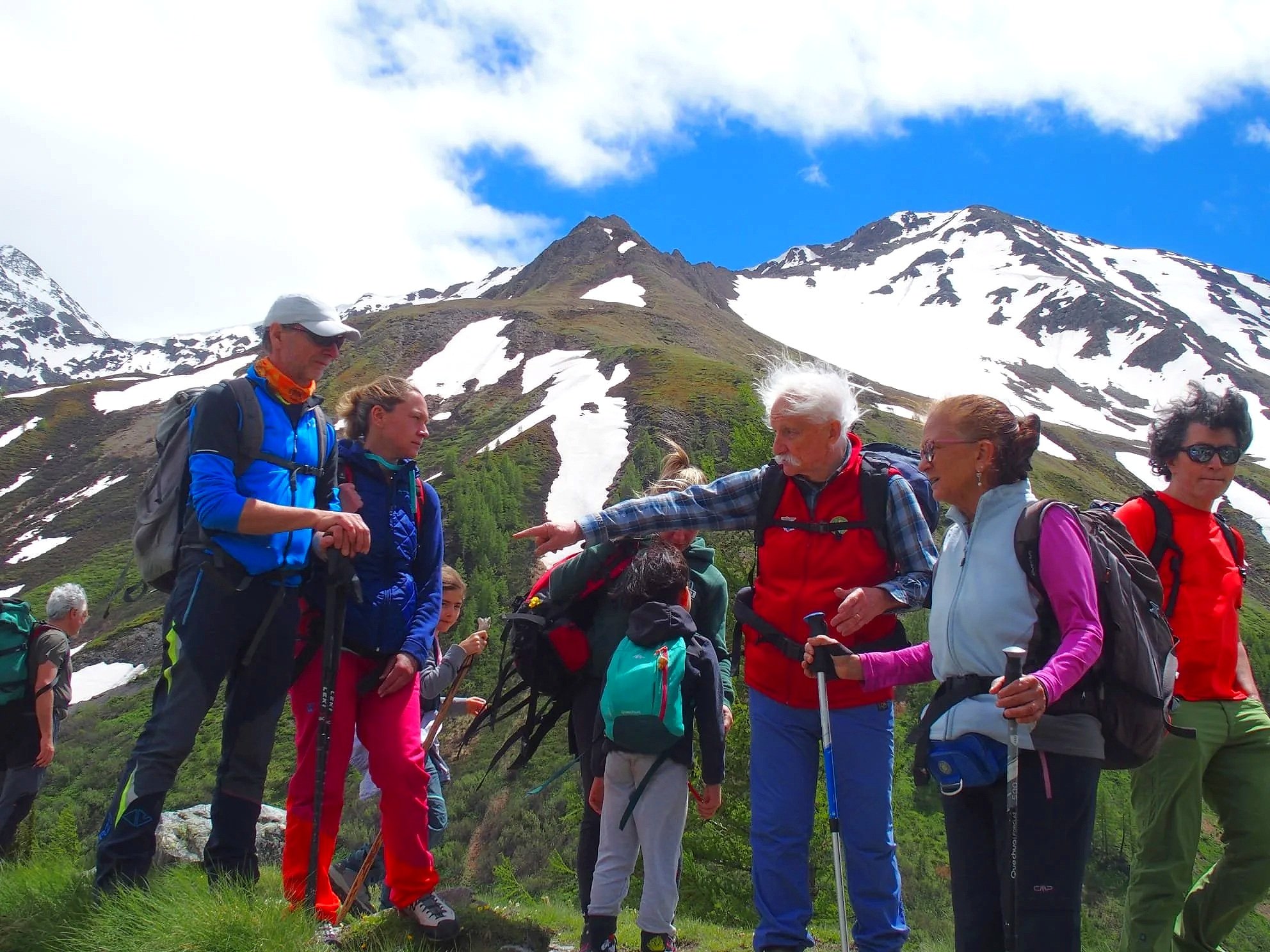 Gruppo di escursionisti su un sentiero in montagna, con neve e cielo blu sullo sfondo.