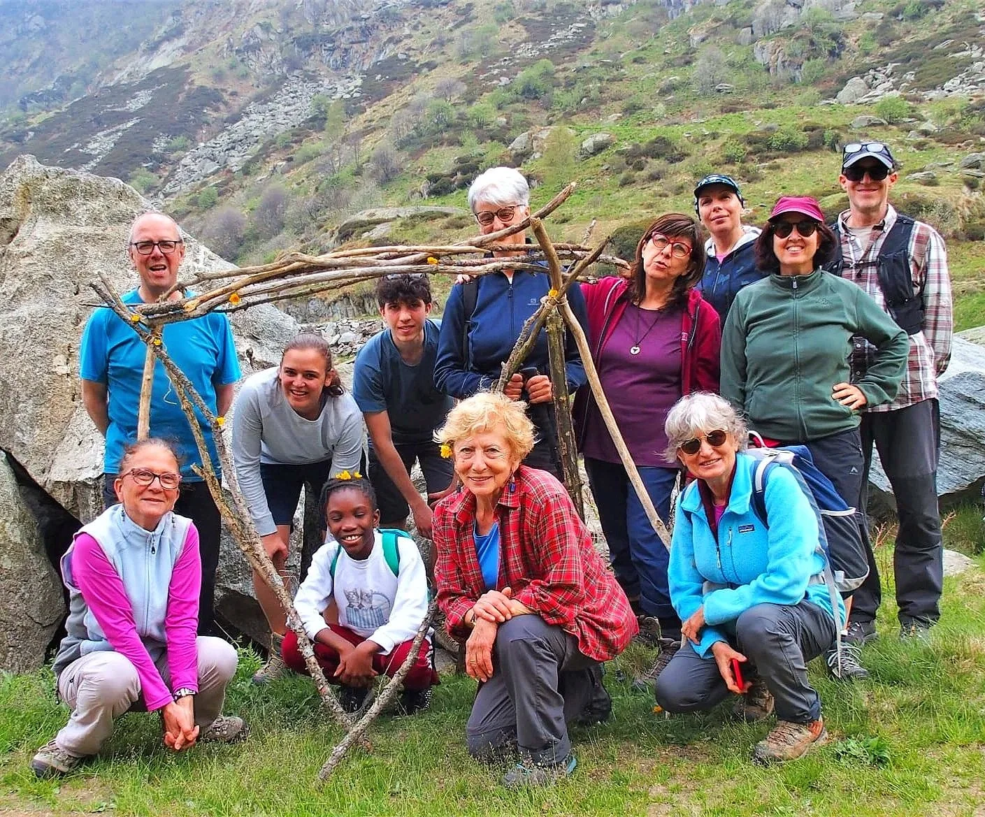 Gruppo di persone durante un'escursione in montagna, con un quadro di rami di alberi decorati con fiorellini gialli.