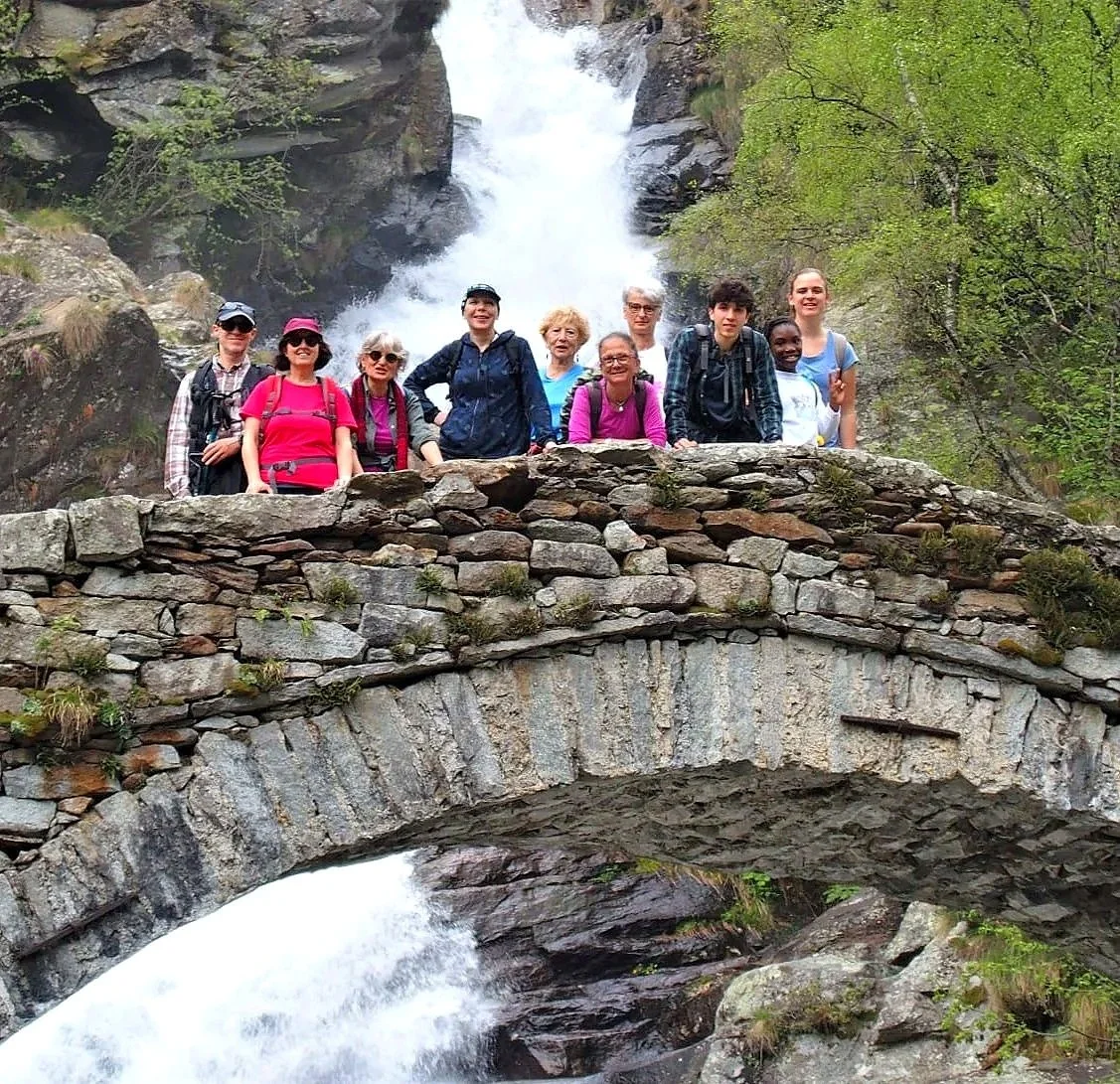 Gruppo di persone che si trovano su un ponte di pietra nel mezzo di una natura con cascate sullo sfondo.