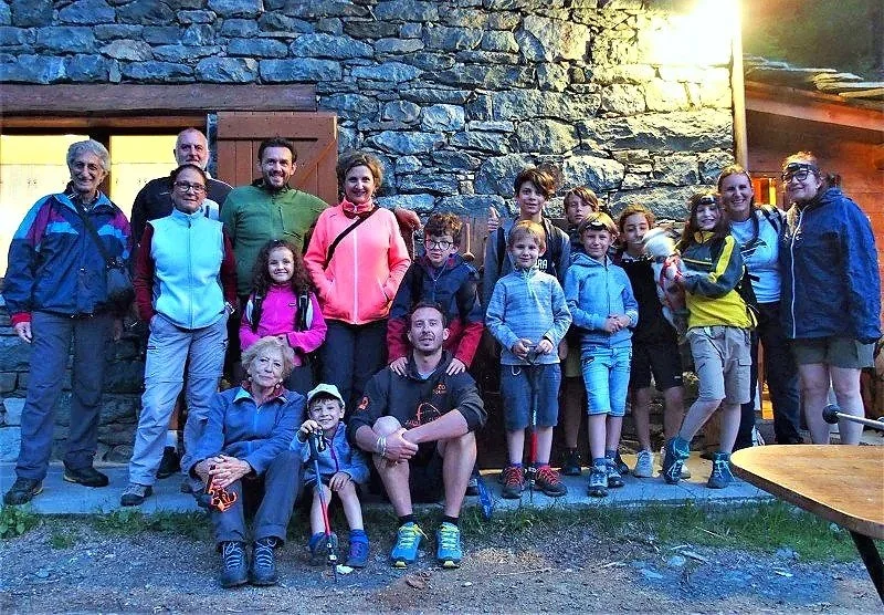 Gruppo di persone, adulti e bambini, che si trovano davanti a una parete di pietra in un ambiente all'aperto, probabilmente durante un'escursione o un evento sociale.