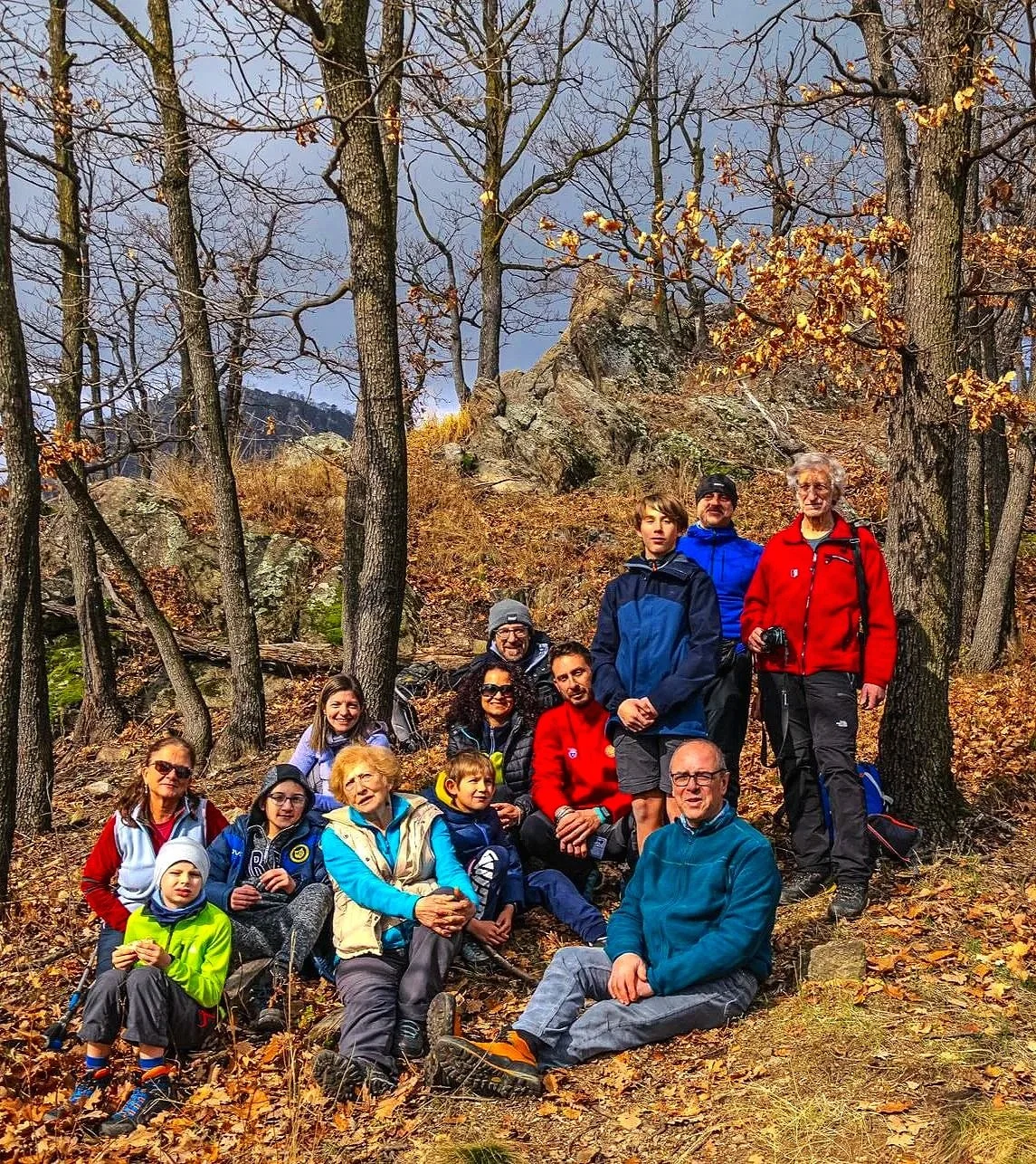 Gruppo di persone in escursione in una foresta autunnale con foglie cadute, alberi e rocce sullo sfondo