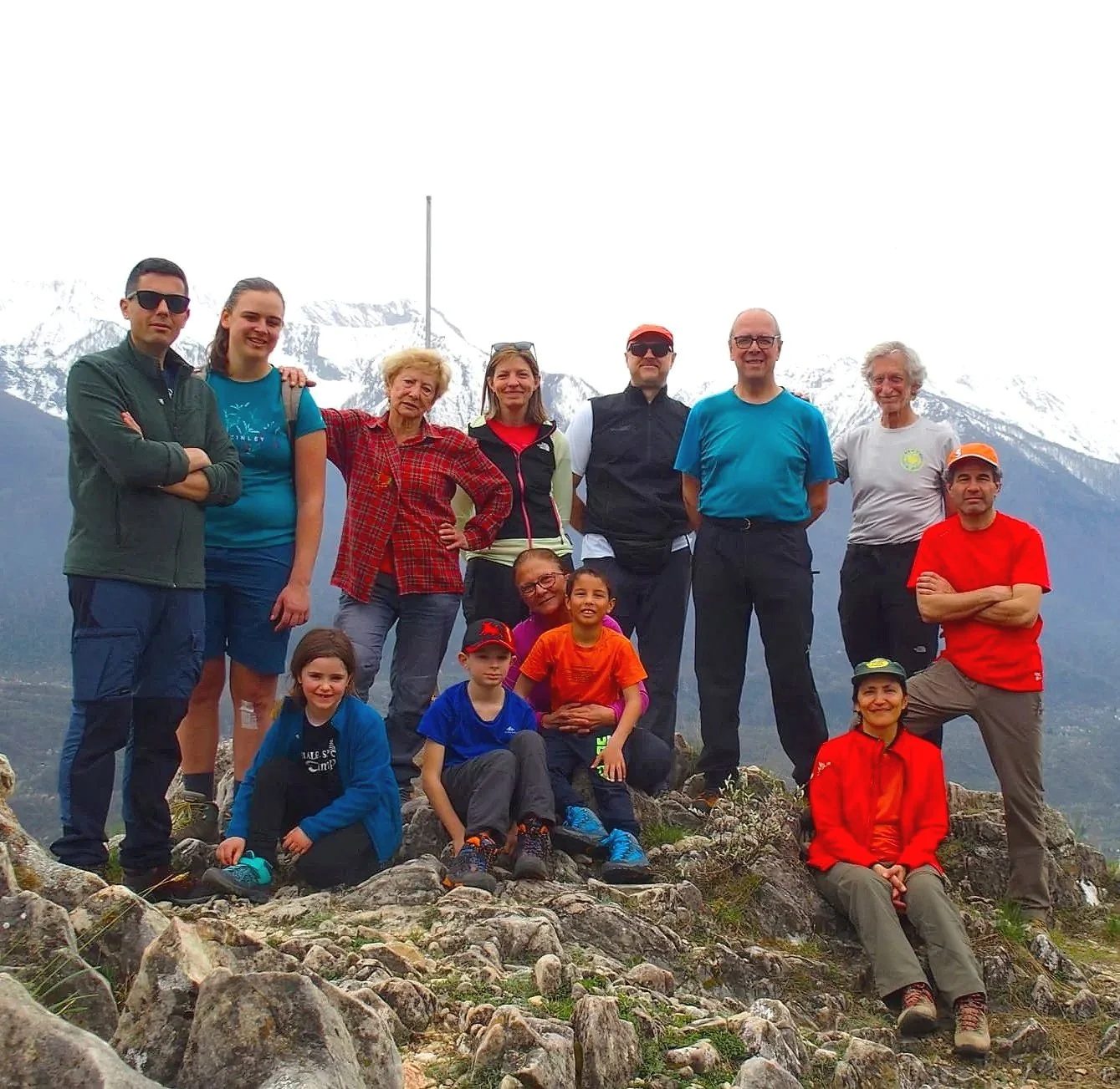 Un gruppo di persone, adulti e bambini, in posa su un sentiero di montagna con le cime innevate sullo sfondo.