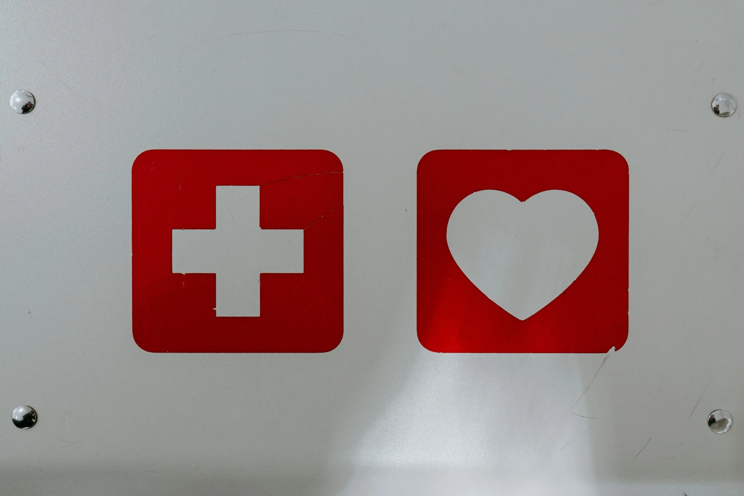 Signs with medical symbols, one with a white cross and one with a heart, on a gray background.