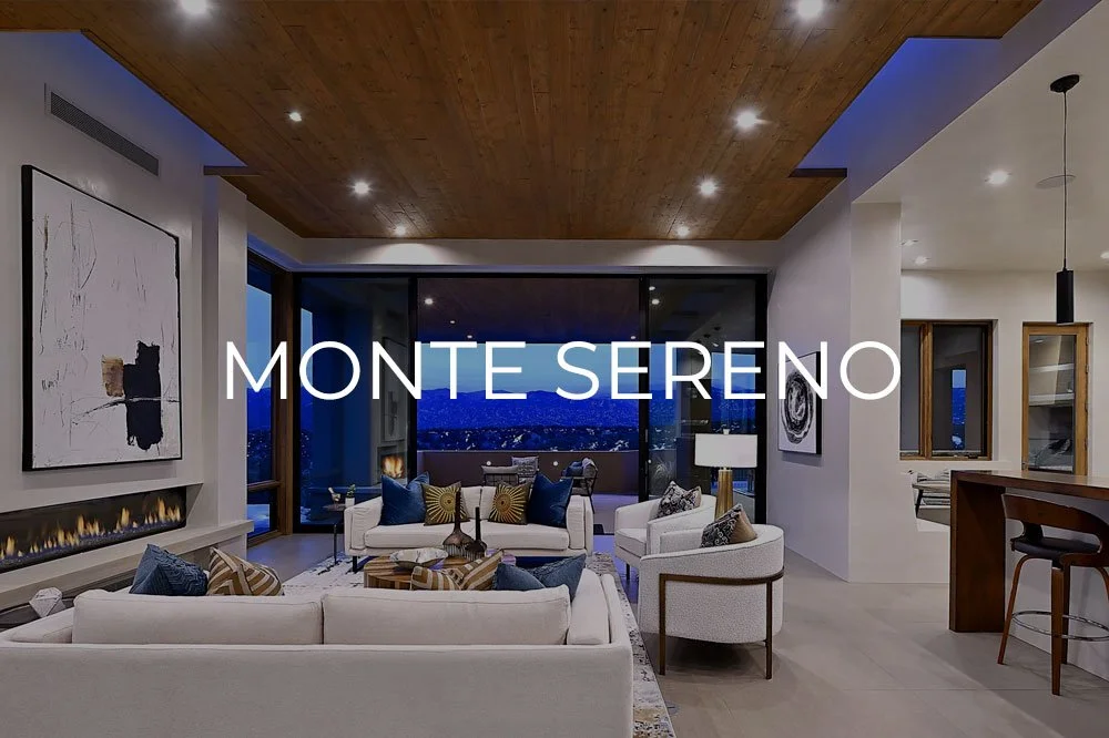 Modern living room with white sofas, colorful pillows, a fireplace, large windows showing a mountain view at night, and wooden ceiling.