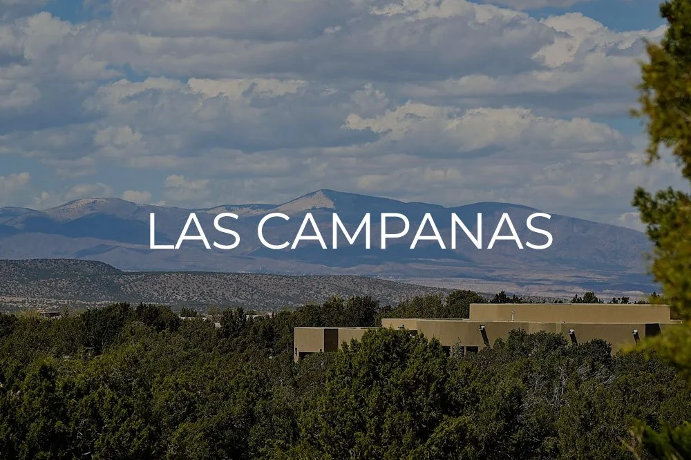 View of mountains and a partly cloudy sky near Las Campanas with trees and buildings in the foreground.