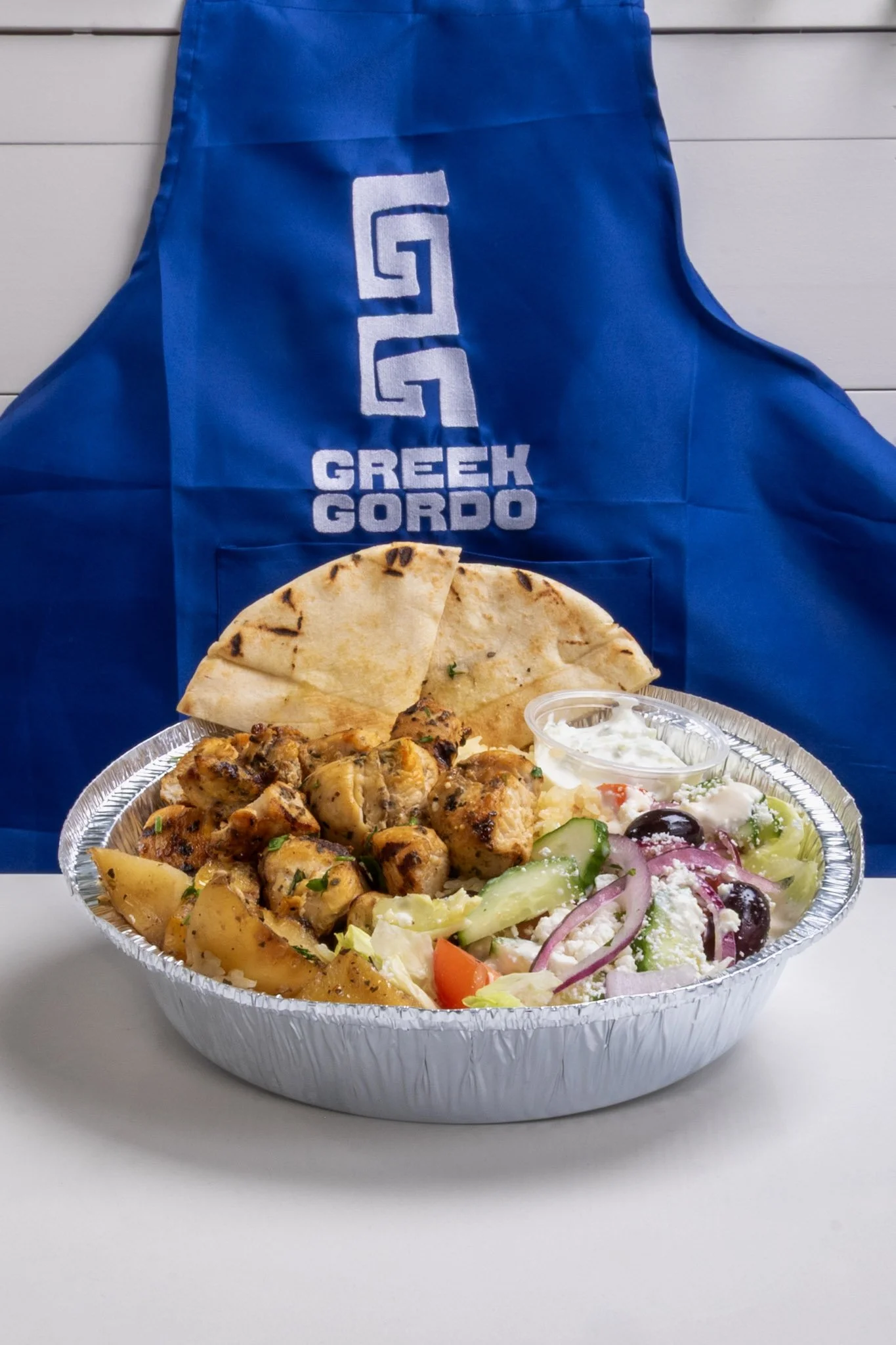 A Greek Gordo grilled chicken, pita bread, Greek salad with cucumbers, tomatoes, red onion, black olives, feta cheese, and tzatziki sauce.