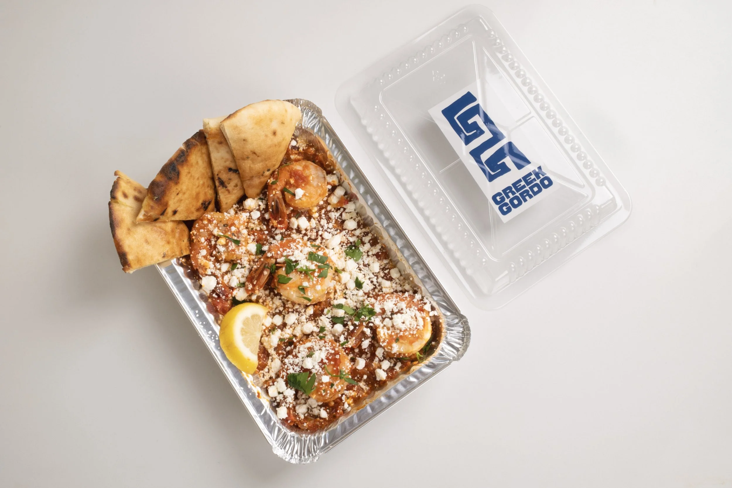 Takeout shrimp in red sauce with cheese and herbs, sliced lemon, and folded bread 