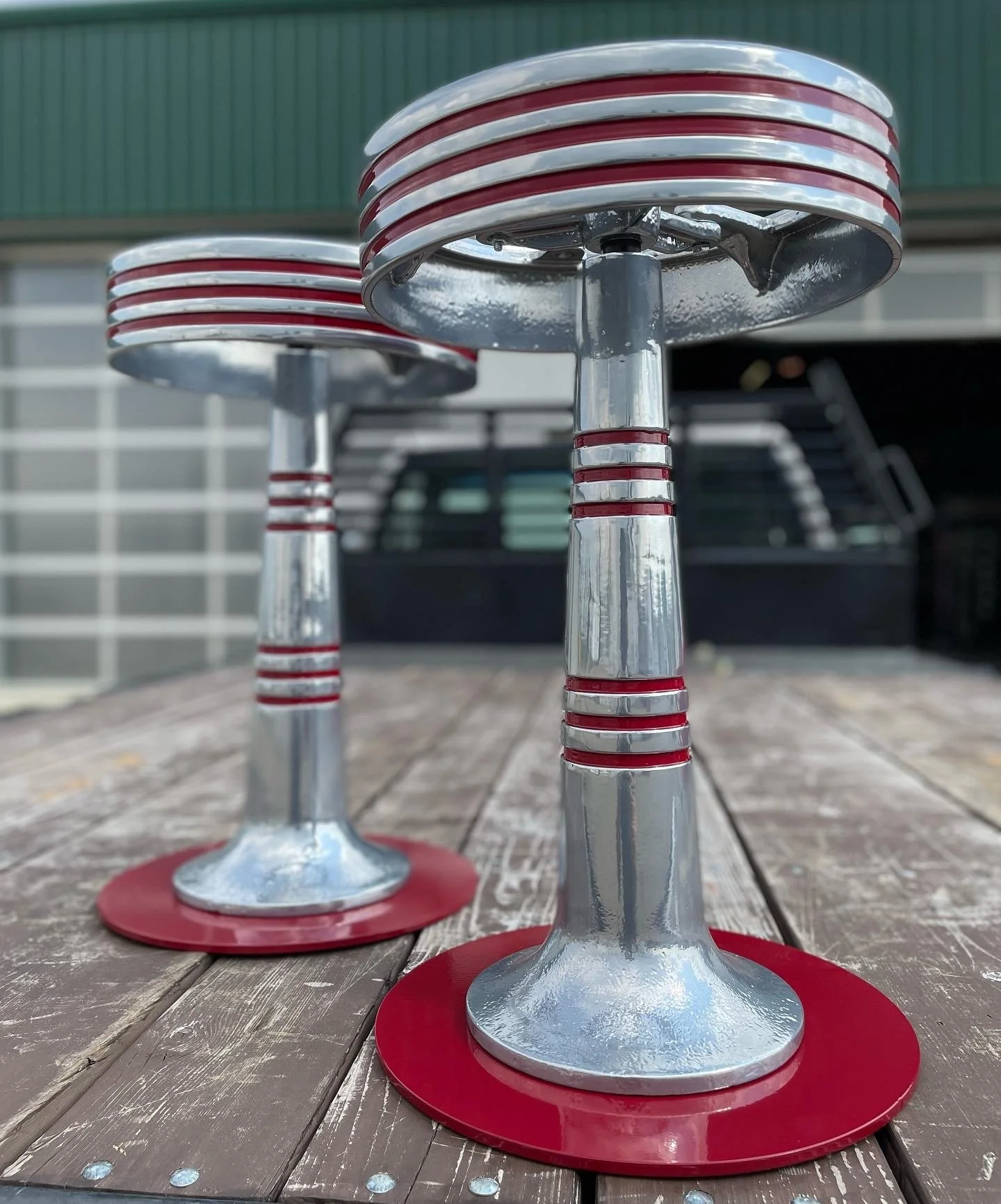 Close-up of two metal stools with red and silver striped design, placed outdoors on a wooden surface.