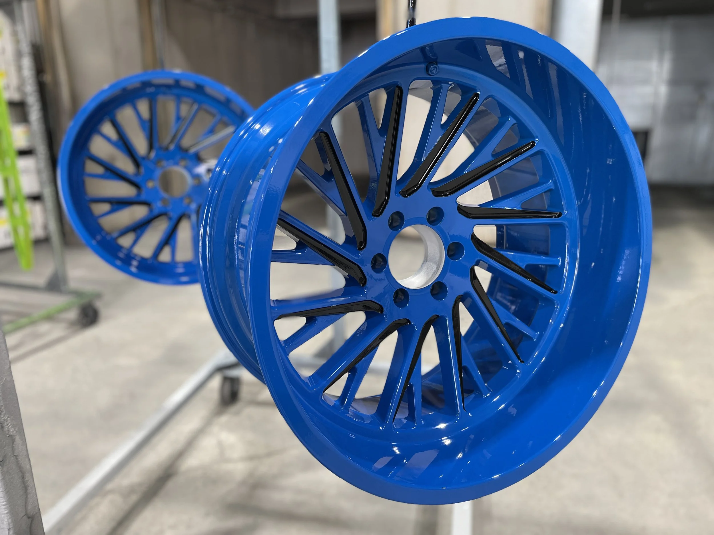 Two blue alloy wheels with black accents hanging on a display rack in a workshop or store.