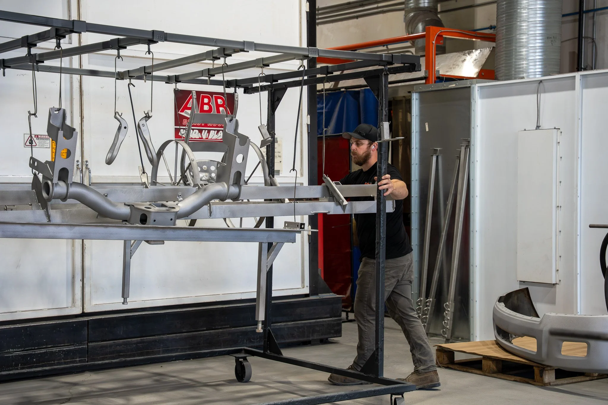 A man working on a metal frame inside a workshop, with various tools and equipment around him.