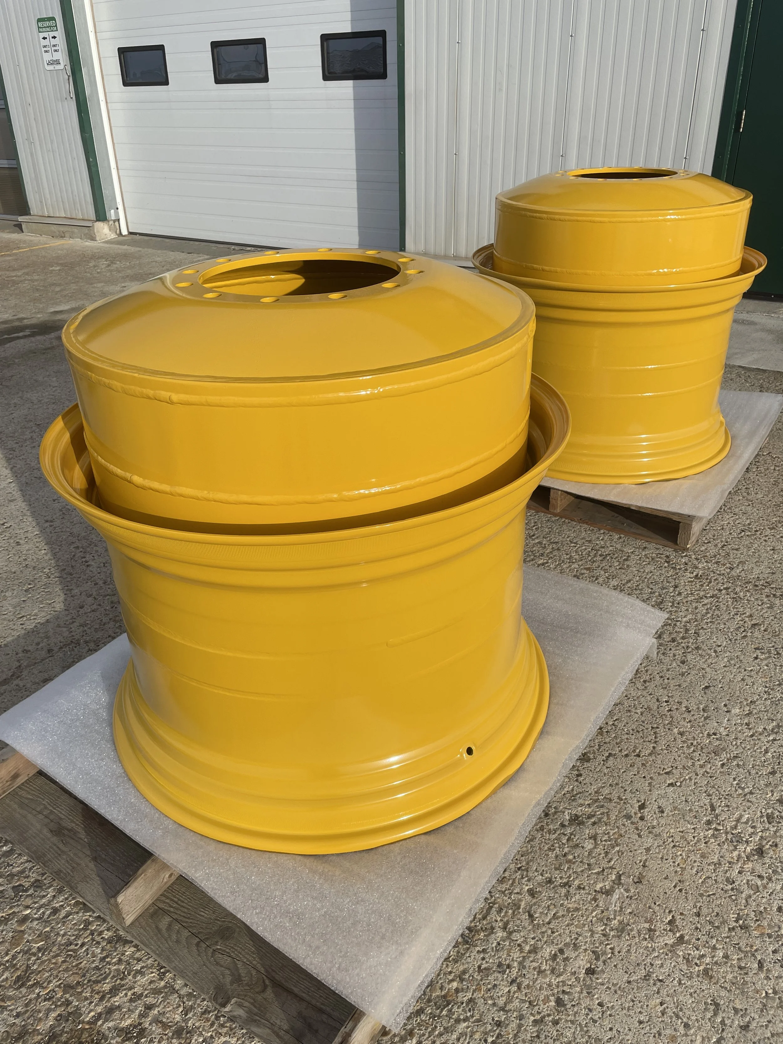 Two large yellow metal wheels stacked on wooden pallets outside near a white garage door.