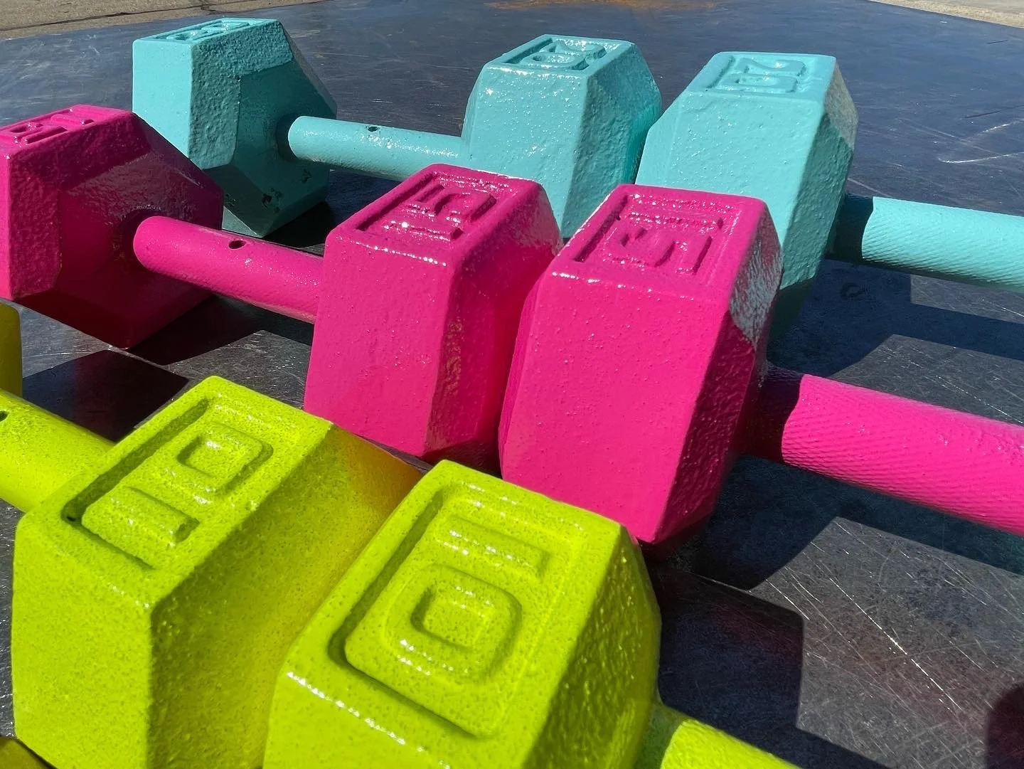 Colorful small dumbbells in pink, yellow, teal, and lime green on a black surface.