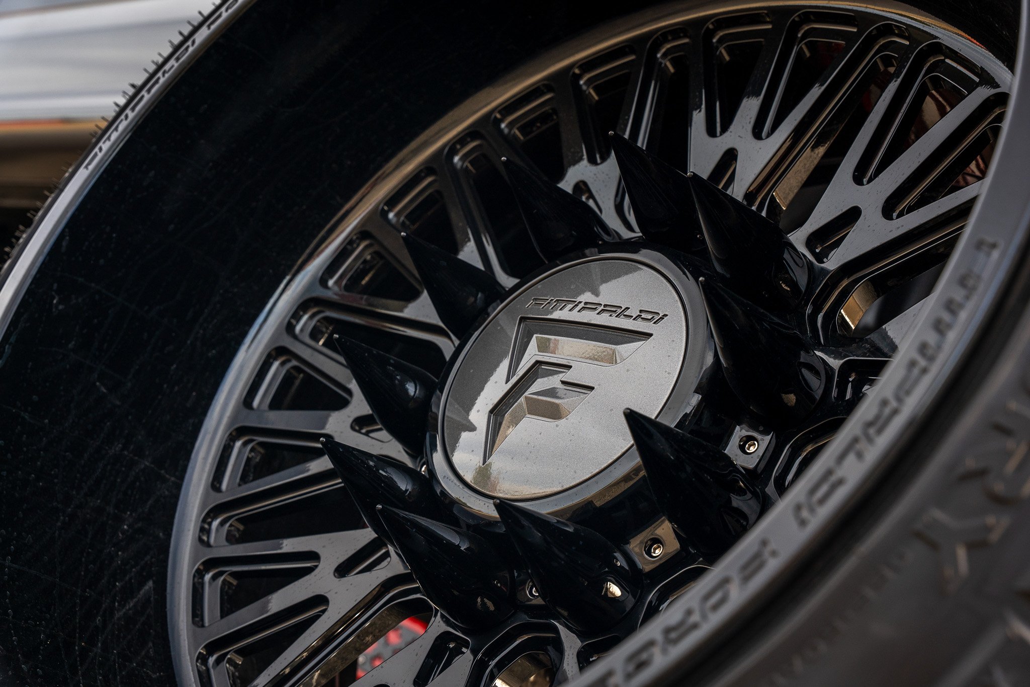 Close-up of a black aftermarket car wheel with a custom center cap featuring a stylized 'F' logo and the brand name 'Fittipaldi', accented by black spikes around the center.