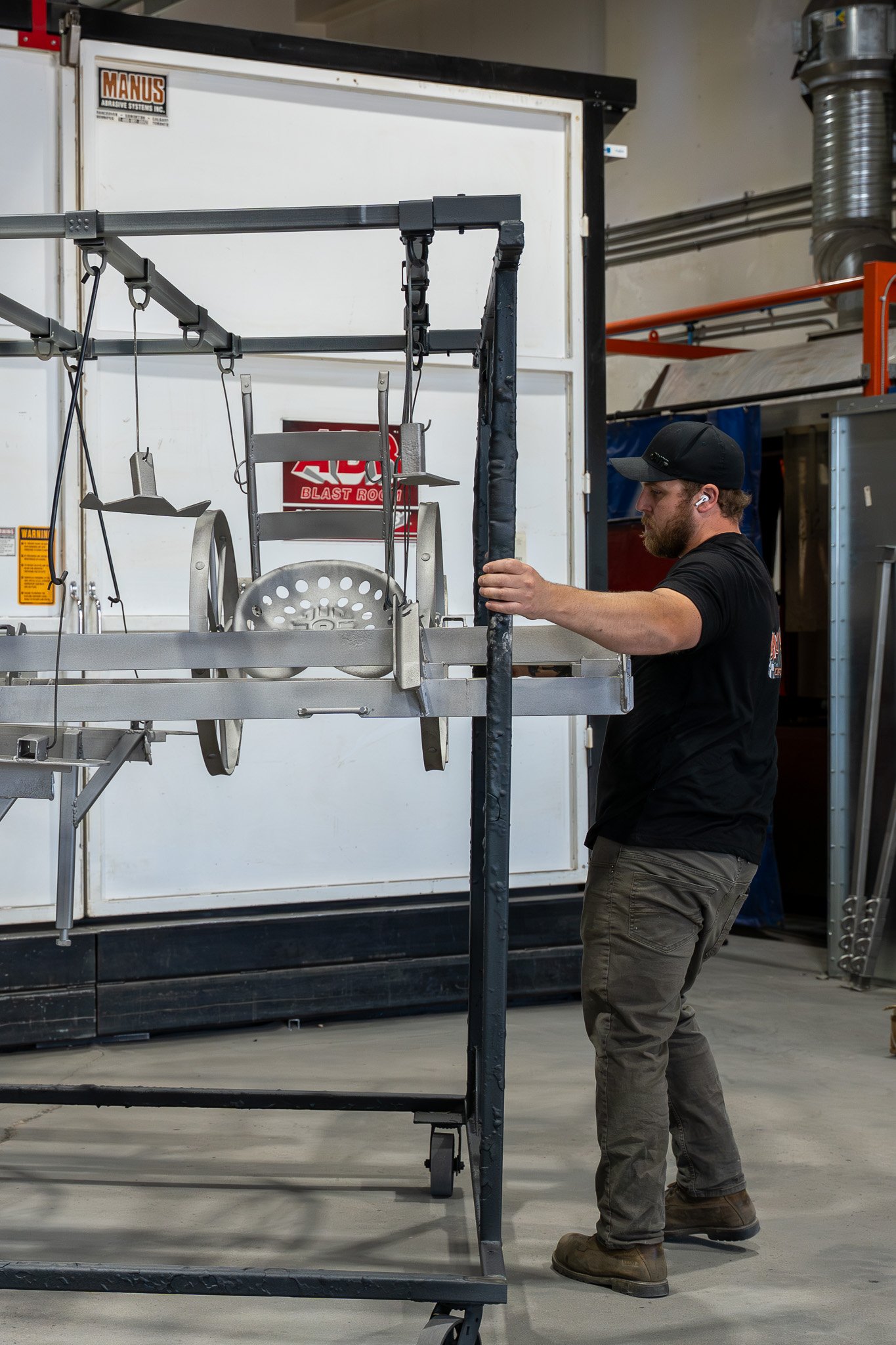 A man in work attire adjusting a metal frame with swing seats in a workshop or manufacturing setting.
