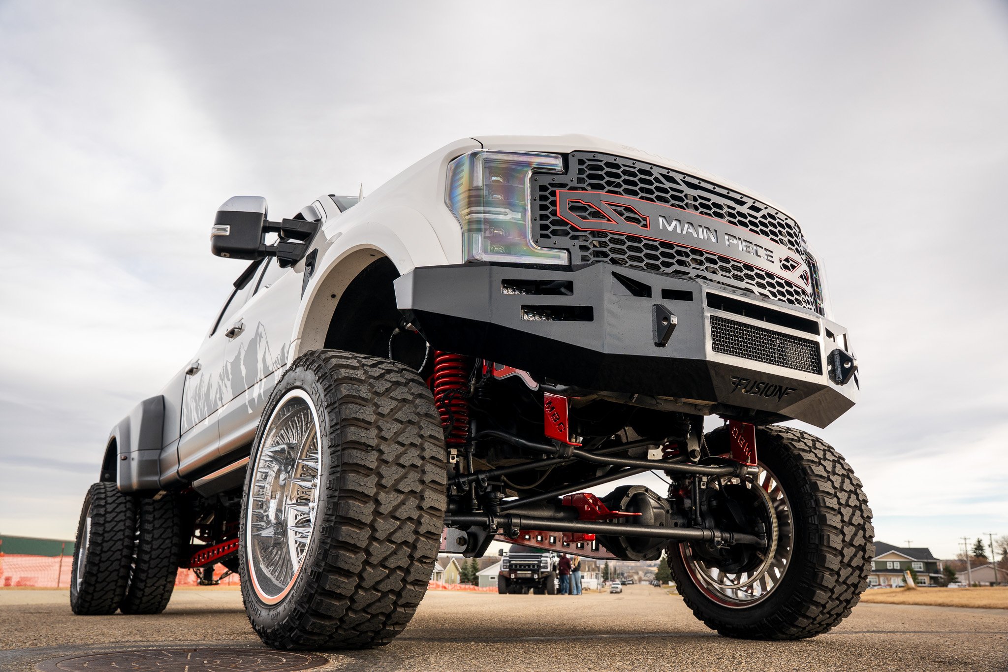 A customized lifted pickup truck with large off-road tires, suspension, and modifications displayed outdoors on a cloudy day.